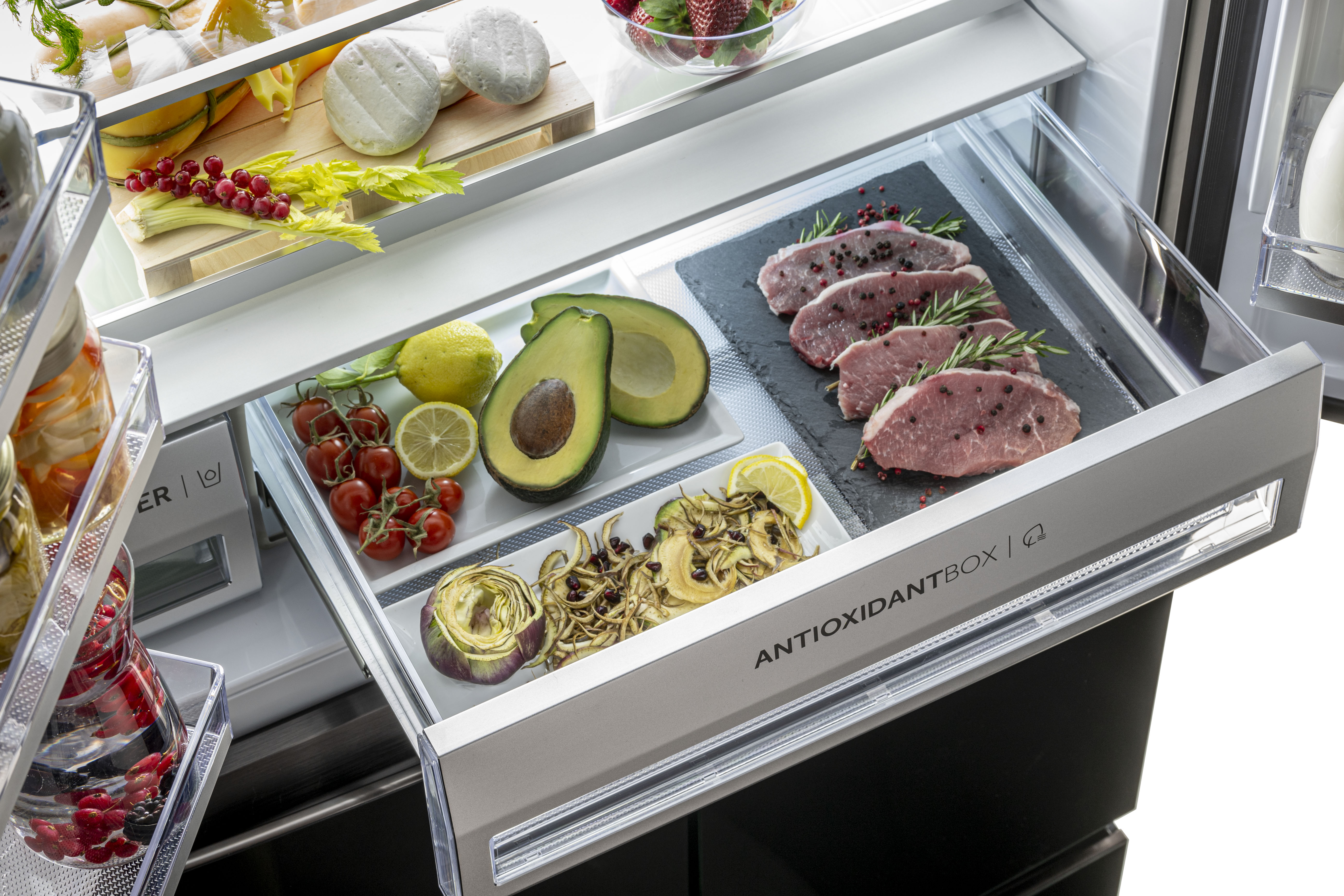 Kühlschrank Schublade mit Essen: Avocado, Steaks, Zitrone, Tomaten, Artischocke und Käse.