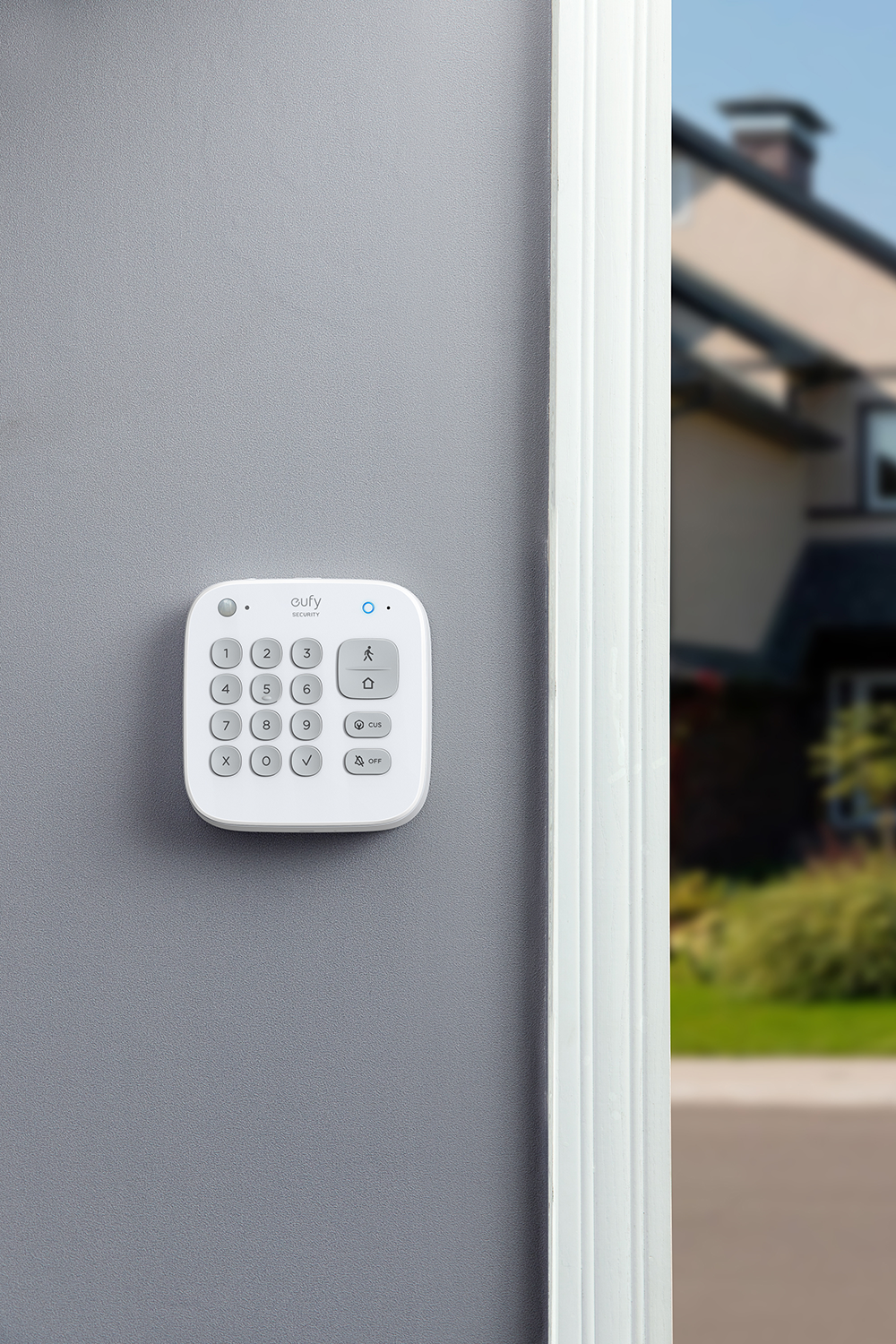 White Eufy keypad security system mounted on a gray wall next to a door frame and house.