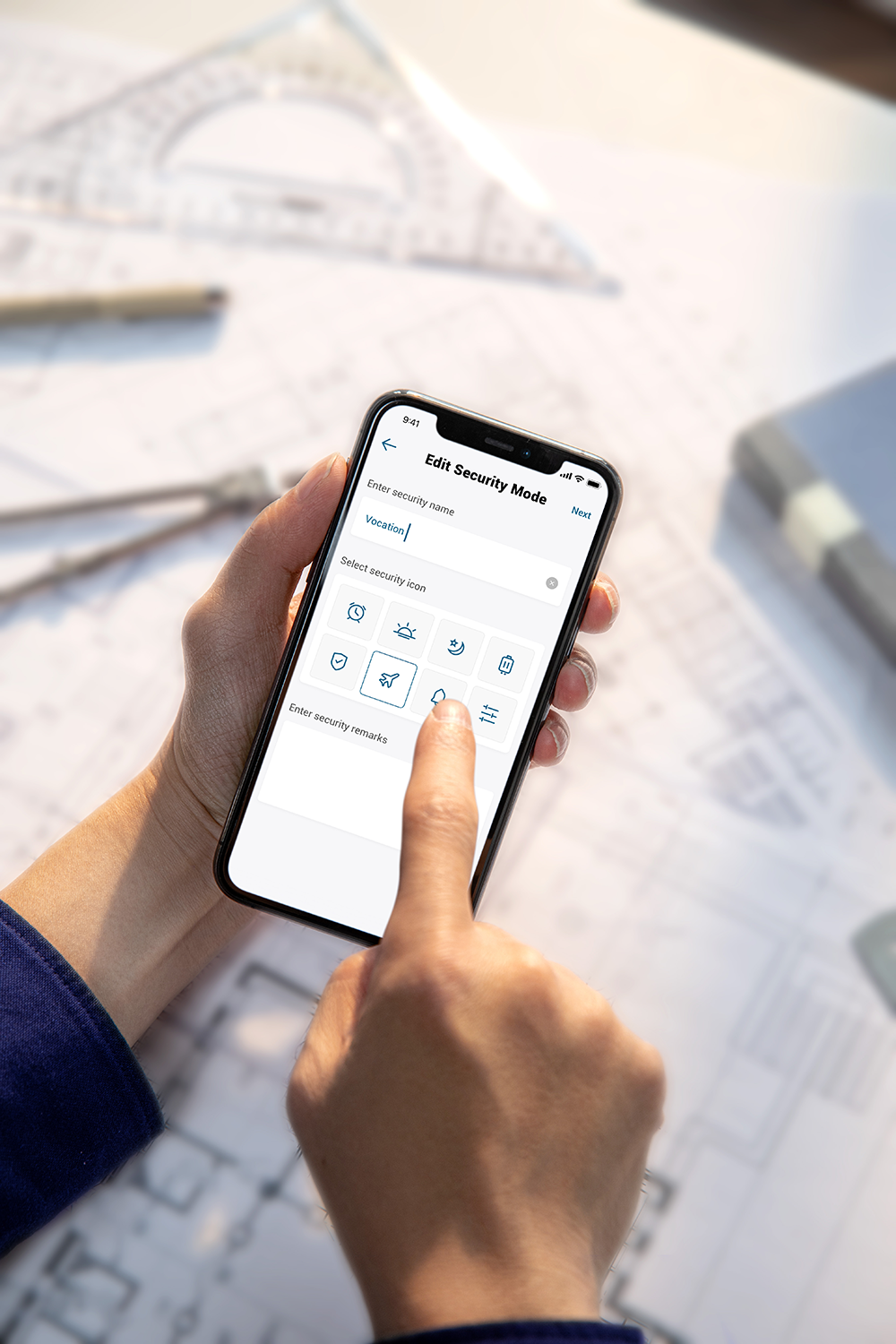 Person using a smartphone to edit the security mode, on a desk with blueprints.