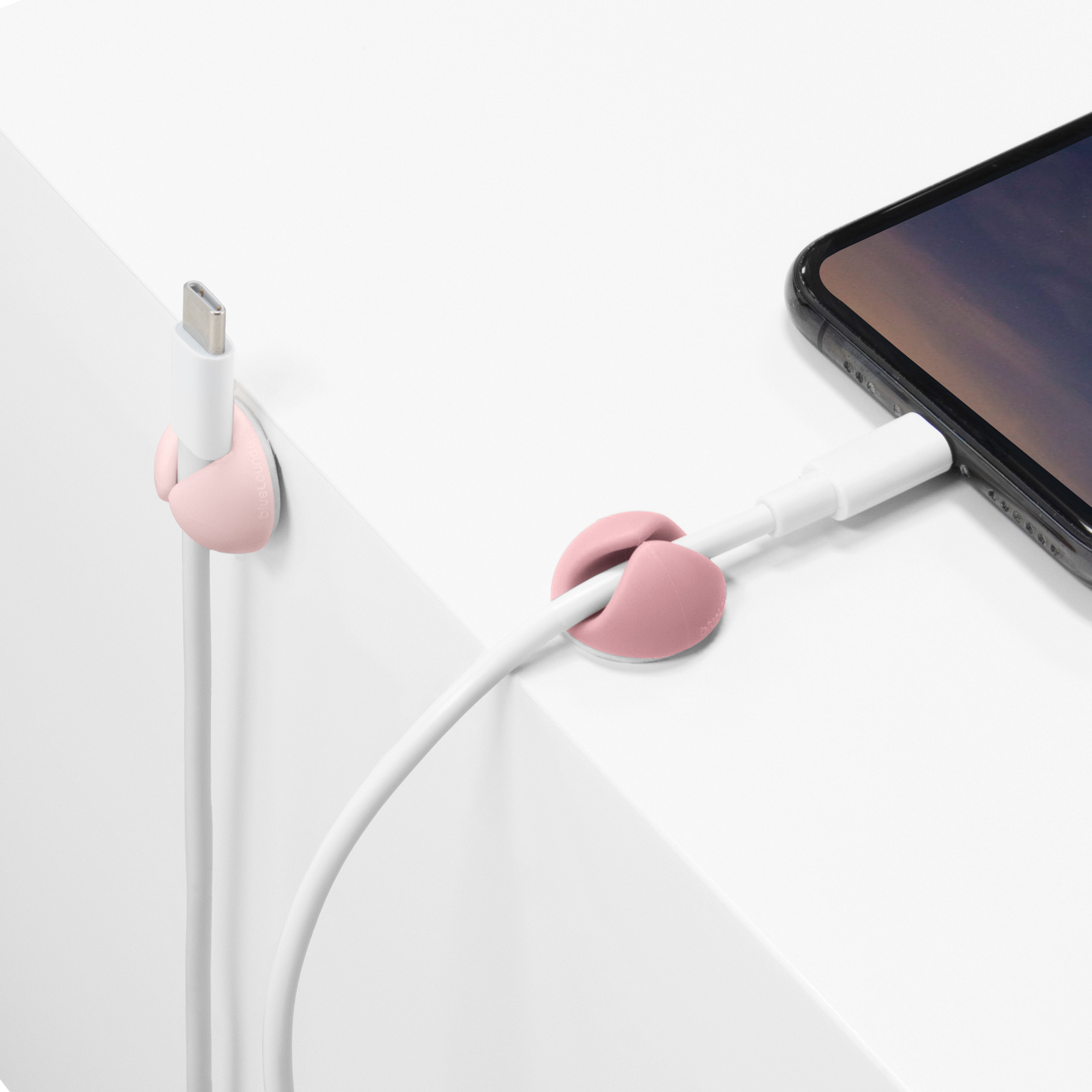 Clip per cavi bianchi che tengono un cavo bianco vicino a un telefono. Supporti rosa su una superficie bianca.