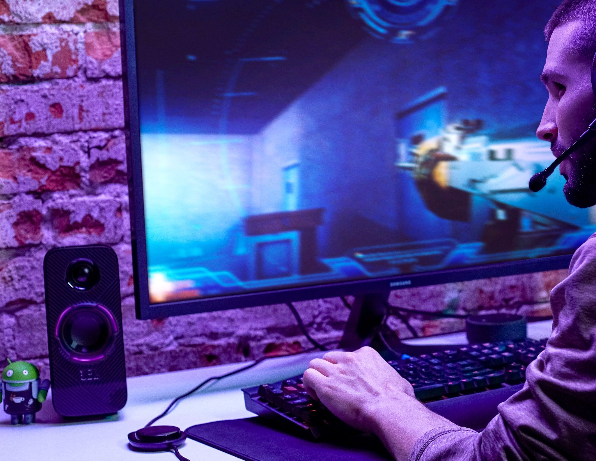 A man gaming, using a keyboard and mouse, with a speaker and monitor on the desk.