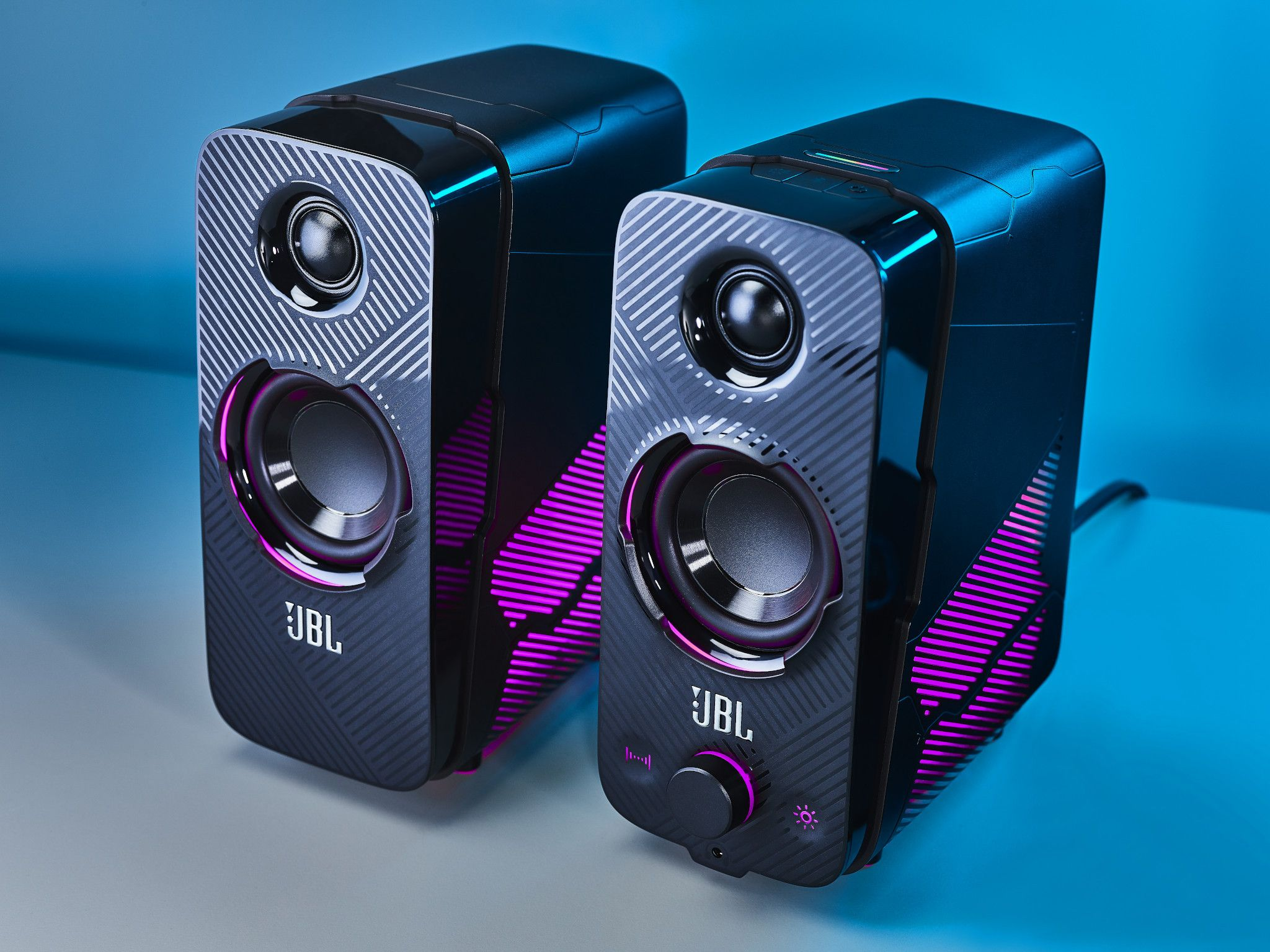 Two black JBL speakers with a unique design. Purple accents. Placed on a blue background.