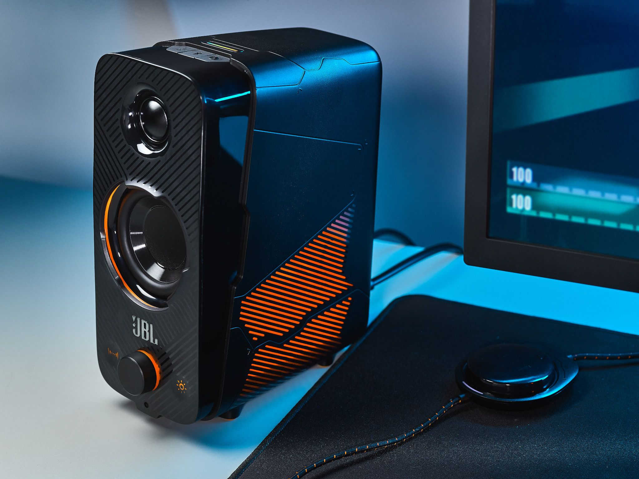 Black and orange JBL speaker with a monitor and mouse pad on a white desk.