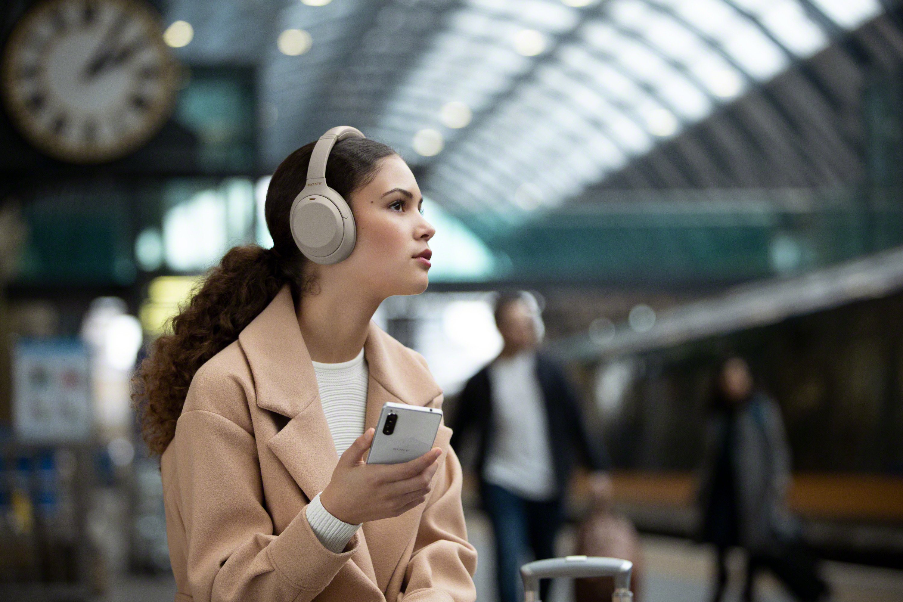 Eine Frau mit Kopfhörern und Telefon, die in einem Bahnhof geht.