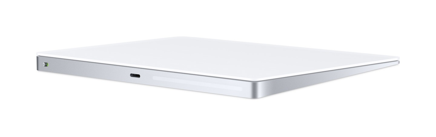 Apple Magic Trackpad blanco sobre fondo blanco. Bordes plateados y puerto de carga visibles.