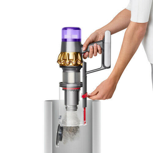 Eine Person bedient einen Dyson-Staubsauger. Der Staubsauger ist silber, gold und lila. Der Staubbehälter wird geleert.