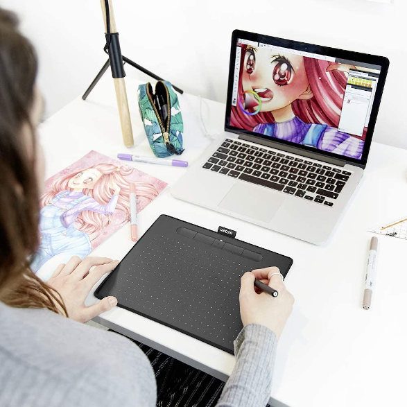 Személy táblagépen rajzol. A laptop művészetet mutat. Rajzeszközök fehér asztalon. Hátsó nézet.