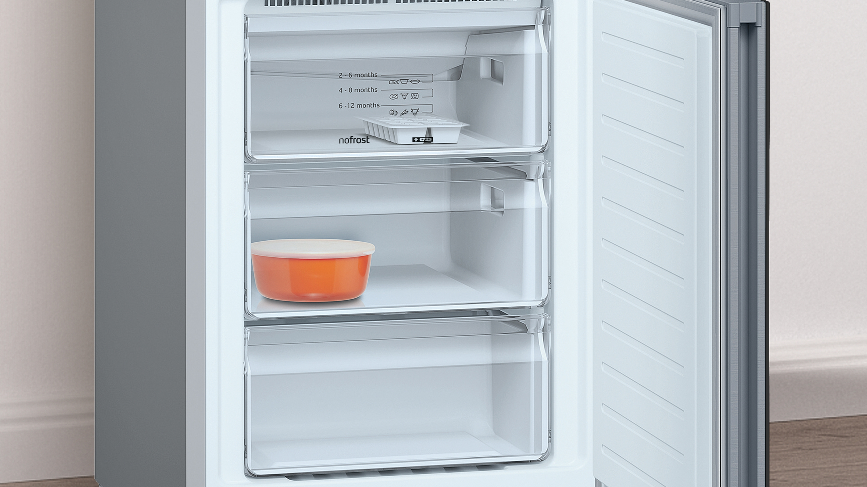 Interior del congelador con dos cajones y un recipiente naranja. Combinación de colores blanco y plata.