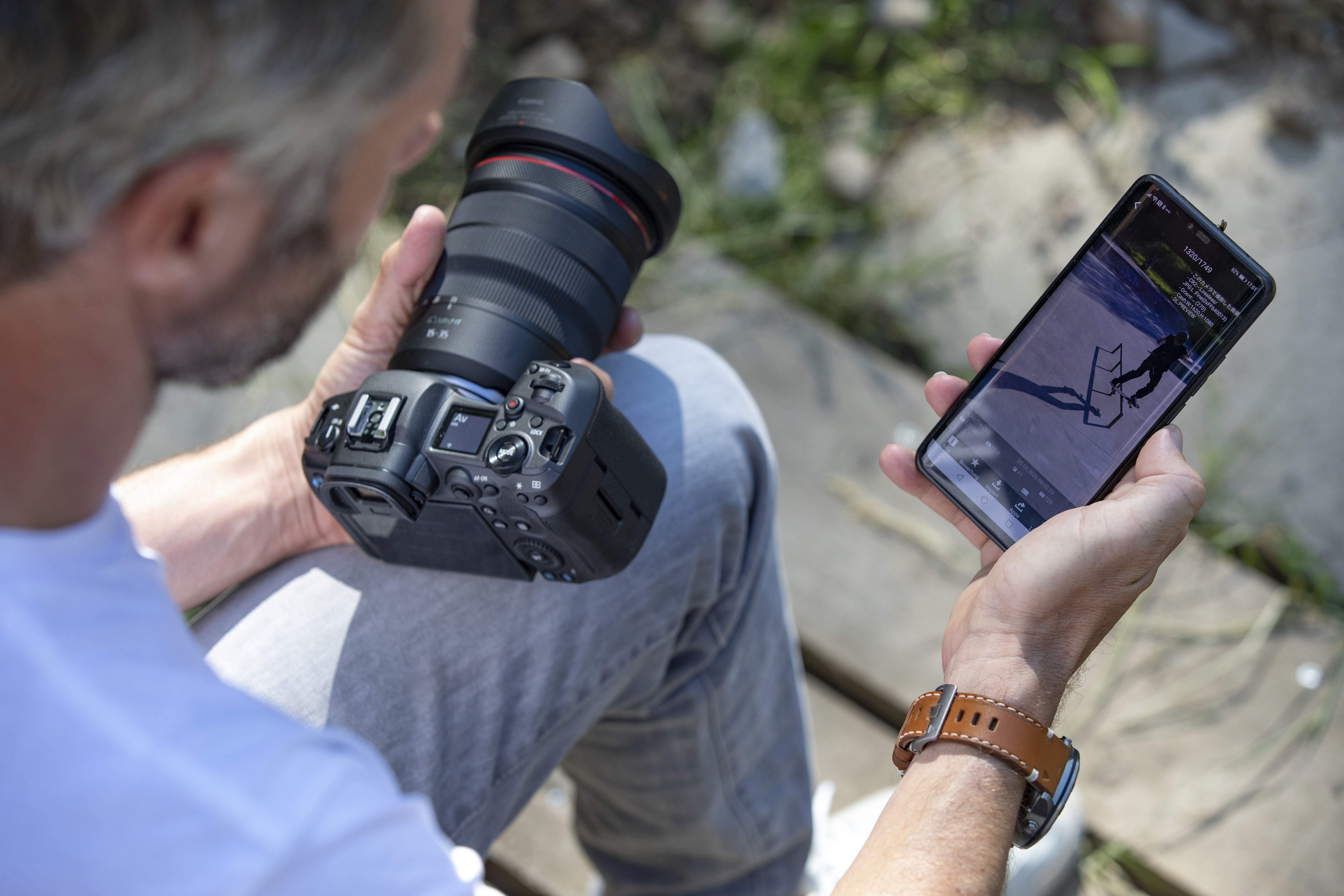 Ein Mann hält eine Kamera und schaut auf einen Smartphone-Bildschirm.