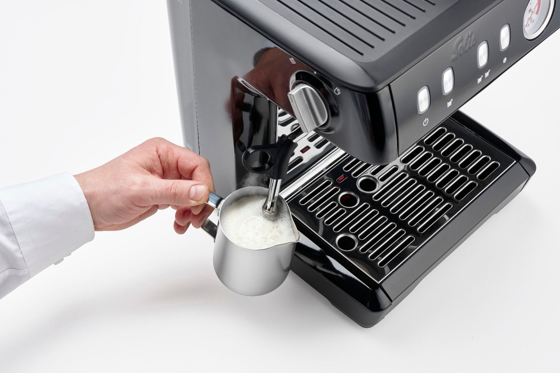 A hand froths milk with the steam wand of a black espresso machine.