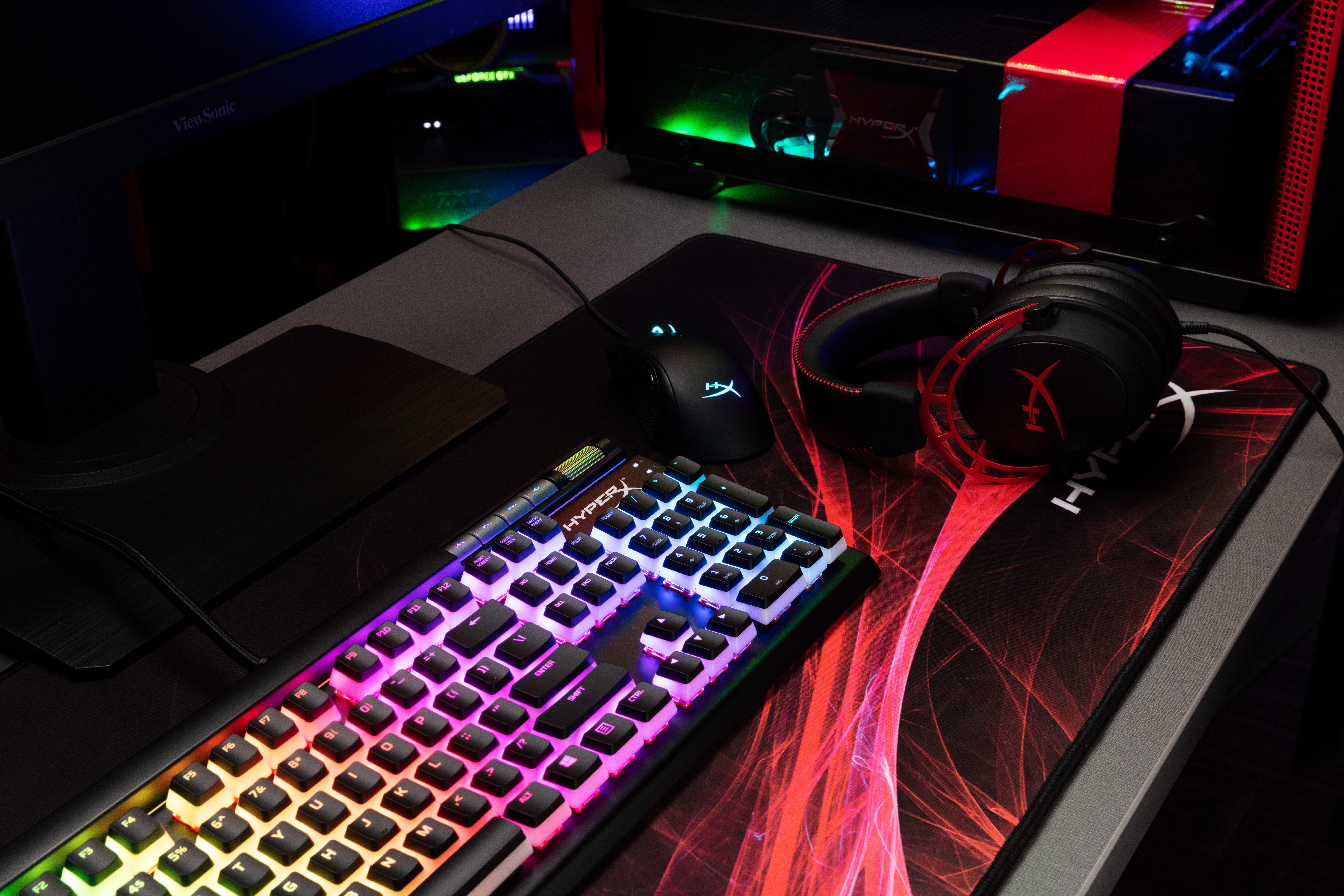 Gaming-Setup: Tastatur mit Regenbogenlichtern, Maus, Kopfhörer und Computer.