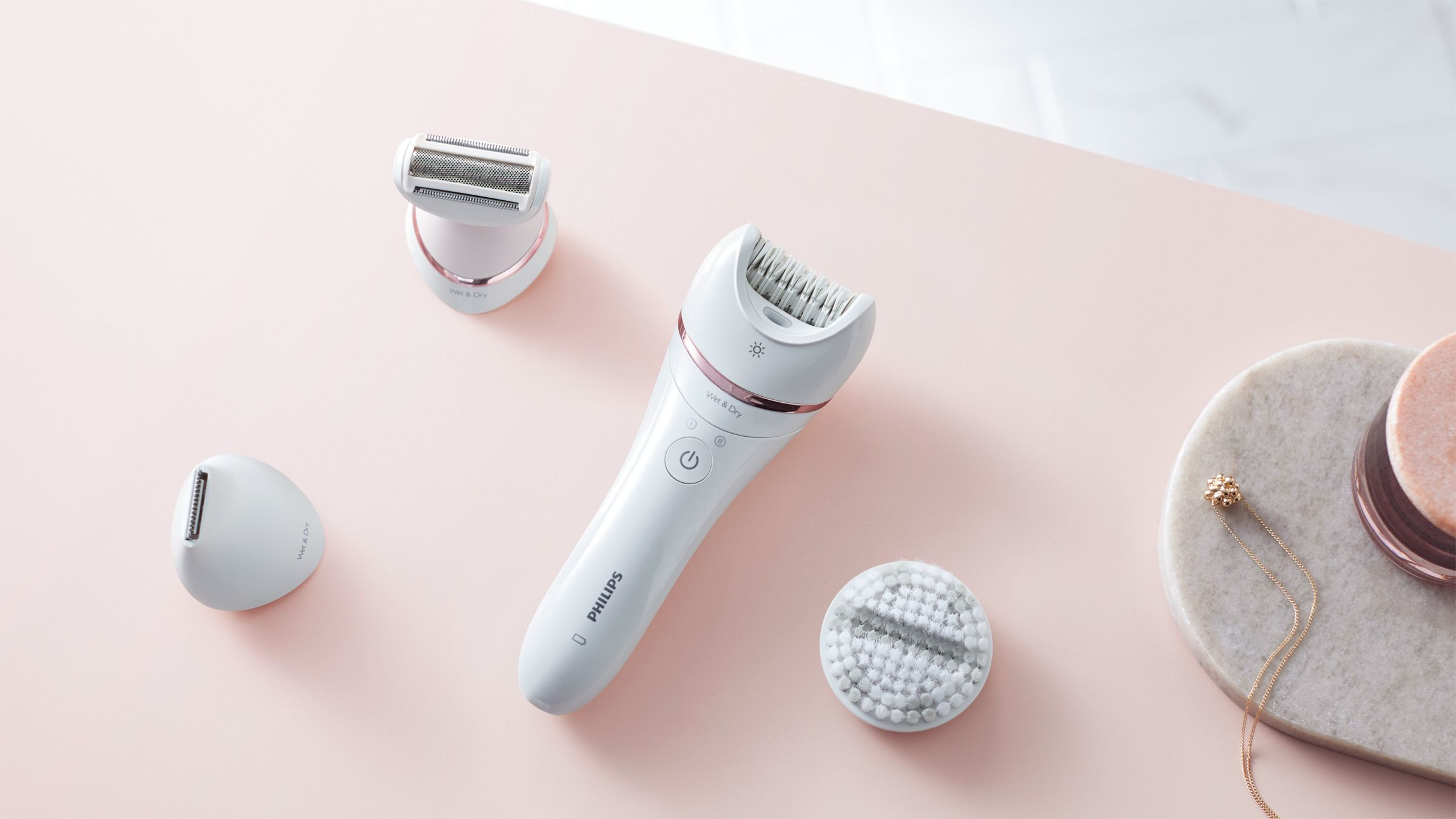Weißer Philips Epilierer mit drei Aufsätzen. Auf einer rosa Oberfläche platziert.