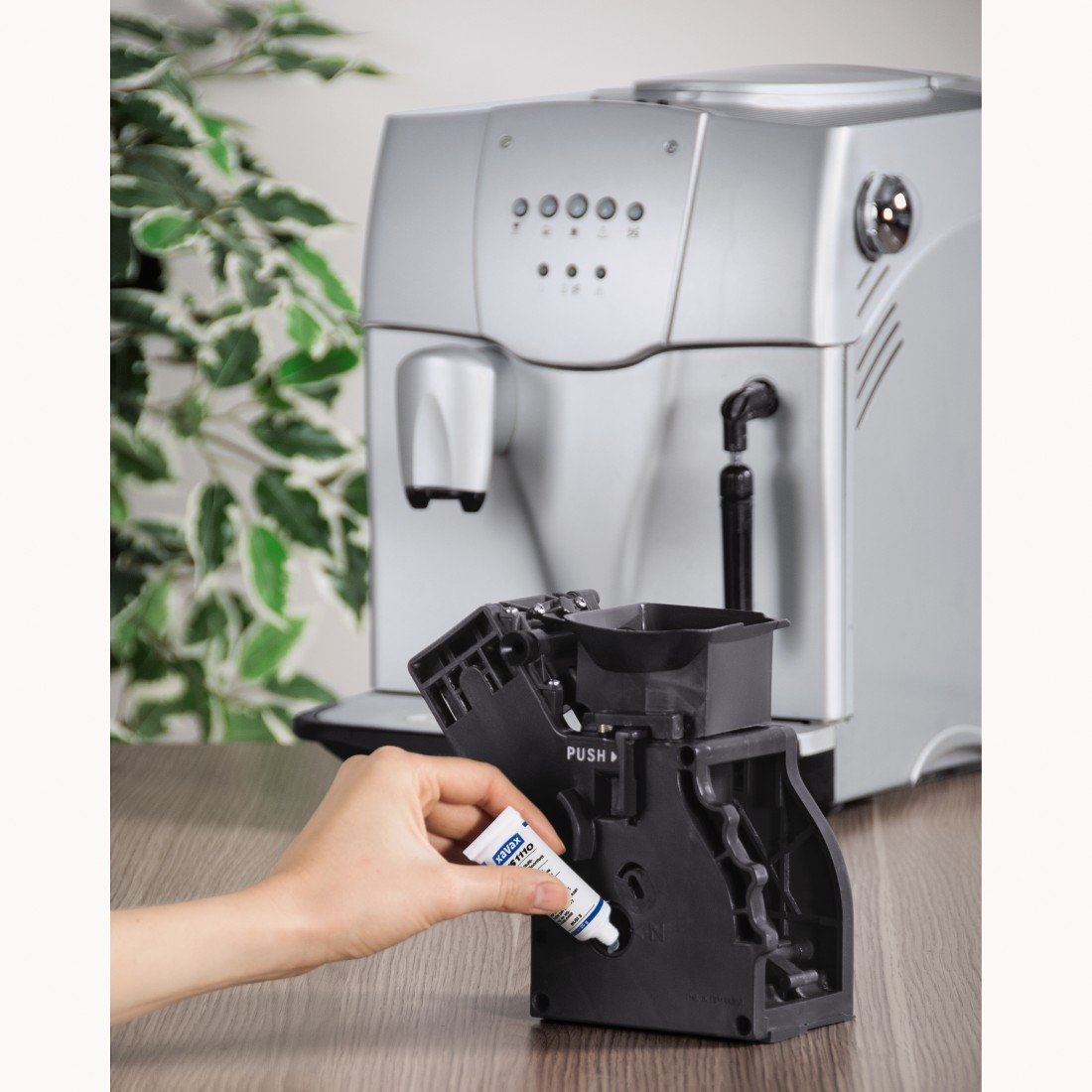 A hand applies grease to a coffee machine component on a table.
