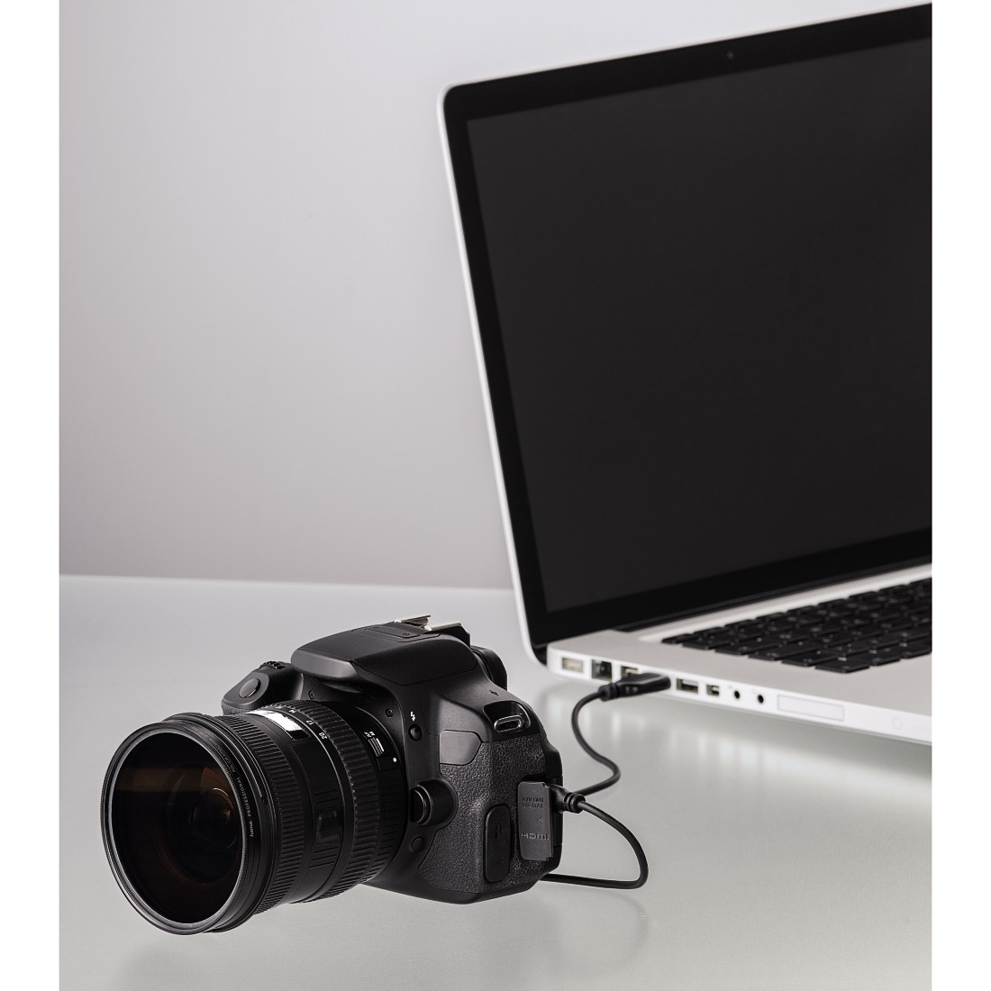 Camera aangesloten op een laptop. De camera is zwart en de laptop is zilver. Wit oppervlak.