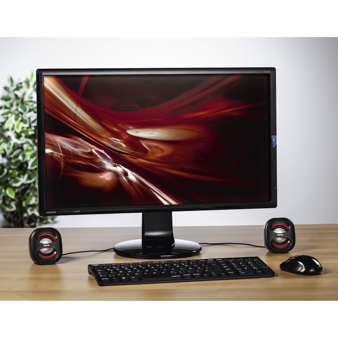Configuration informatique sur table en bois : Écran, haut-parleurs, clavier et souris. Haut-parleurs rouges et noirs.