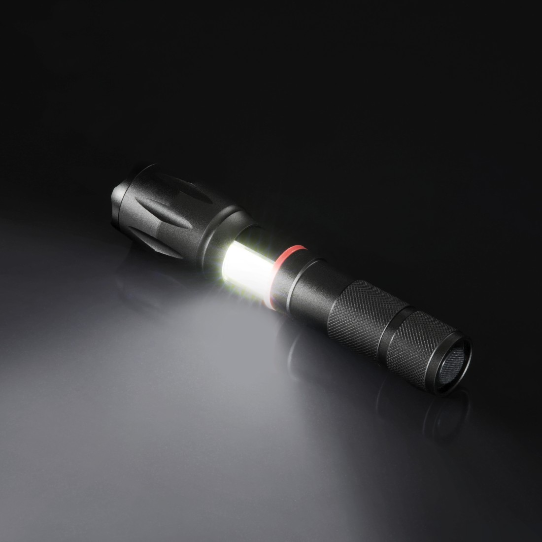Lampe de poche noire avec faisceau lumineux blanc sur surface sombre et réfléchissante.