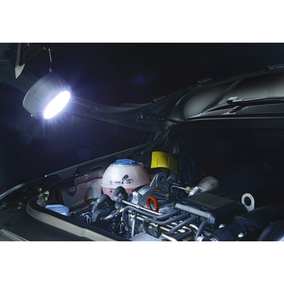 Moteur de voiture éclairé par une lampe de travail suspendue. Le capot est ouvert. Bleu et blanc.
