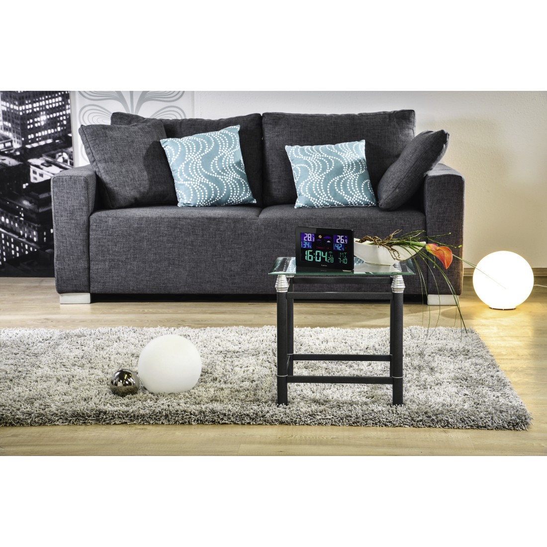 Living room scene with gray sofa, pillows, table with devices, rug, and light.