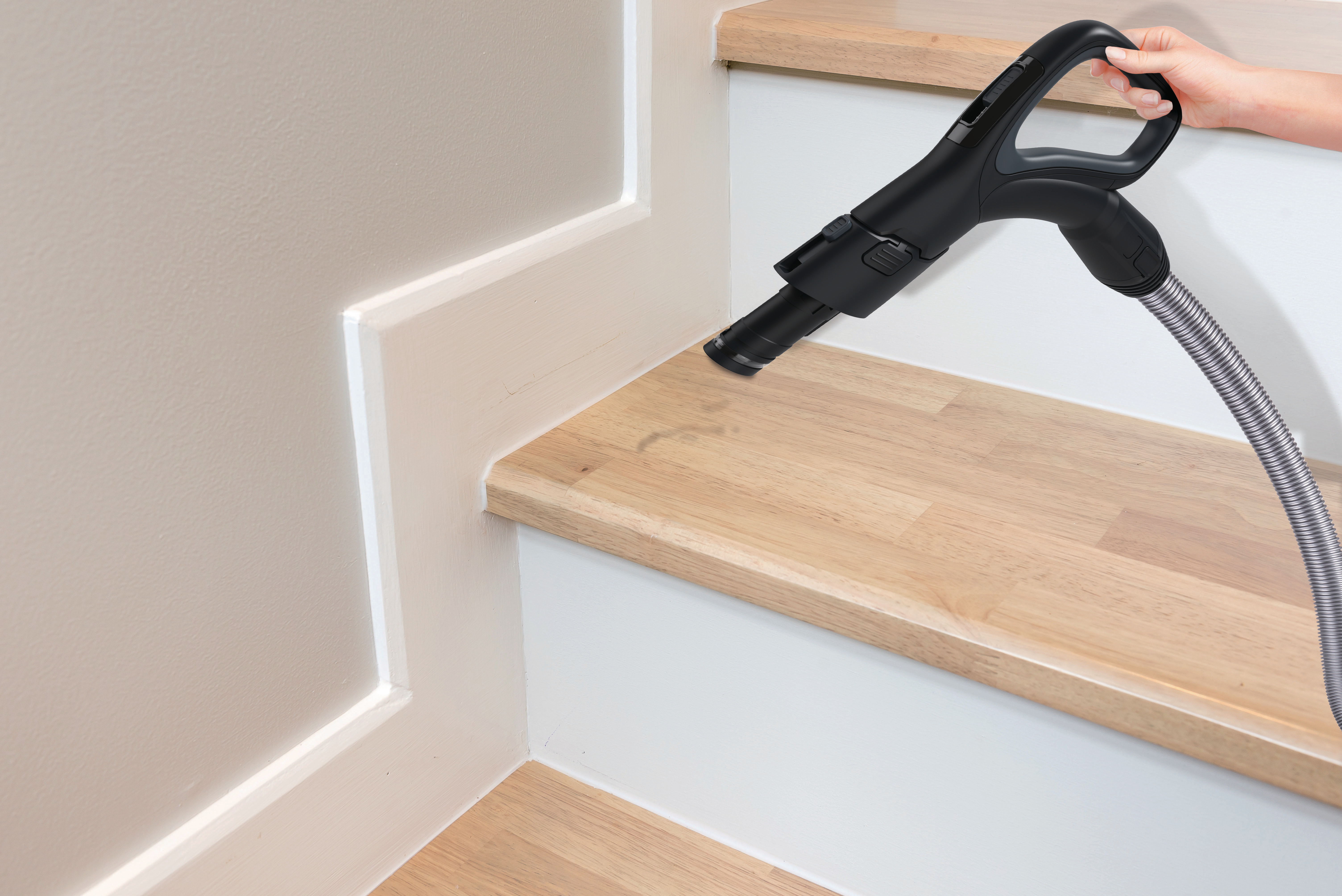 Hand benutzt einen schwarzen Staubsaugeraufsatz, um eine Holztreppe zu reinigen.