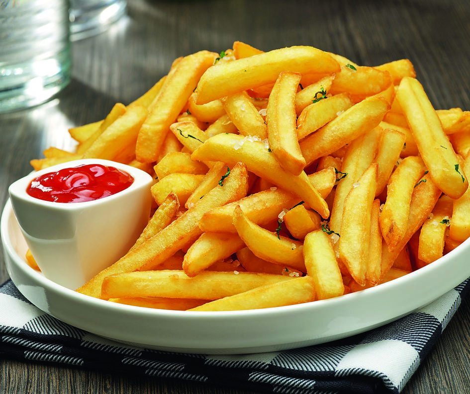Close-up of french fries in a white bowl with a side of red ketchup on a checkered cloth.