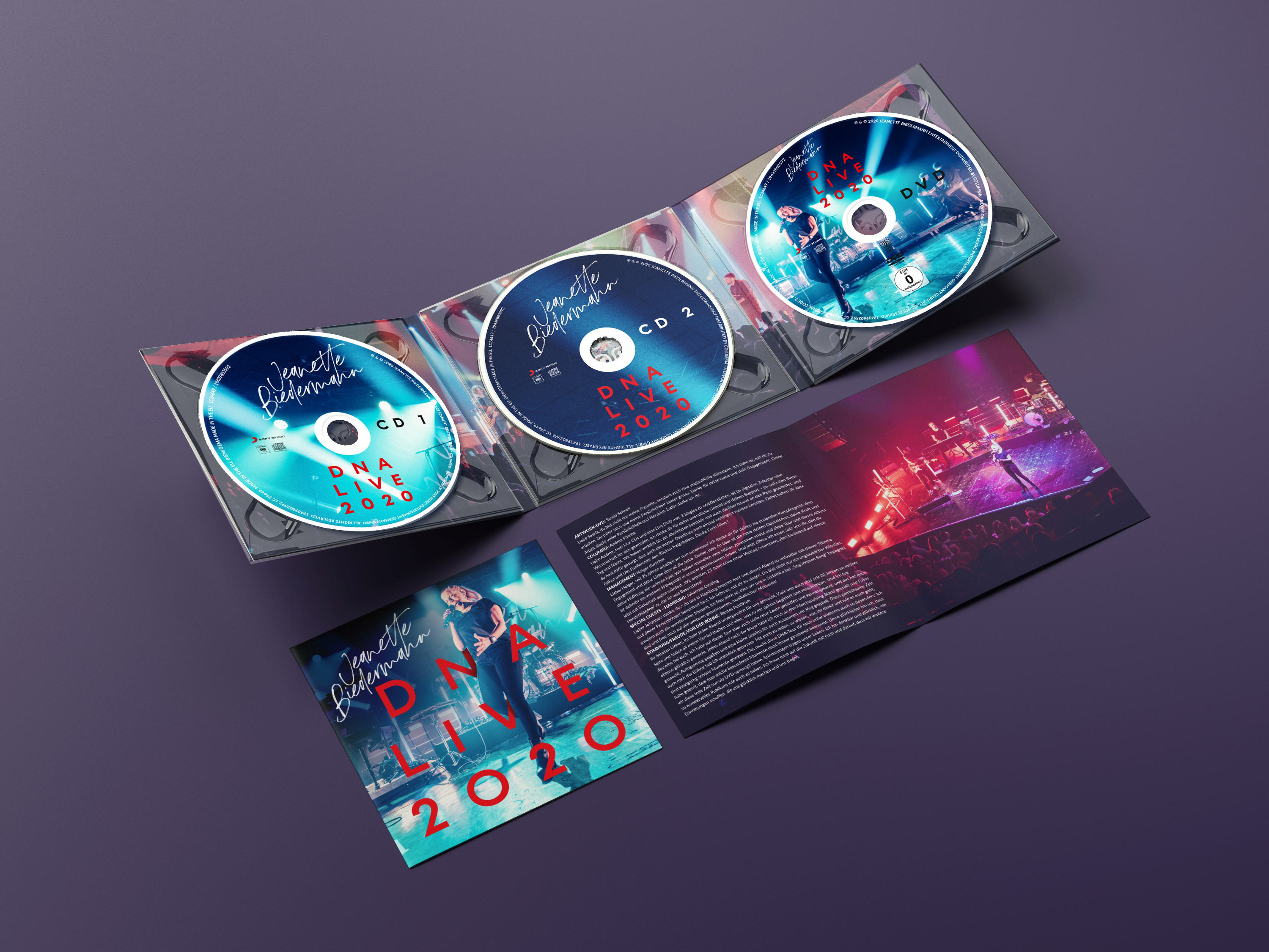 Geöffnete CD-Hülle mit drei Discs und Broschüre auf lila Oberfläche.