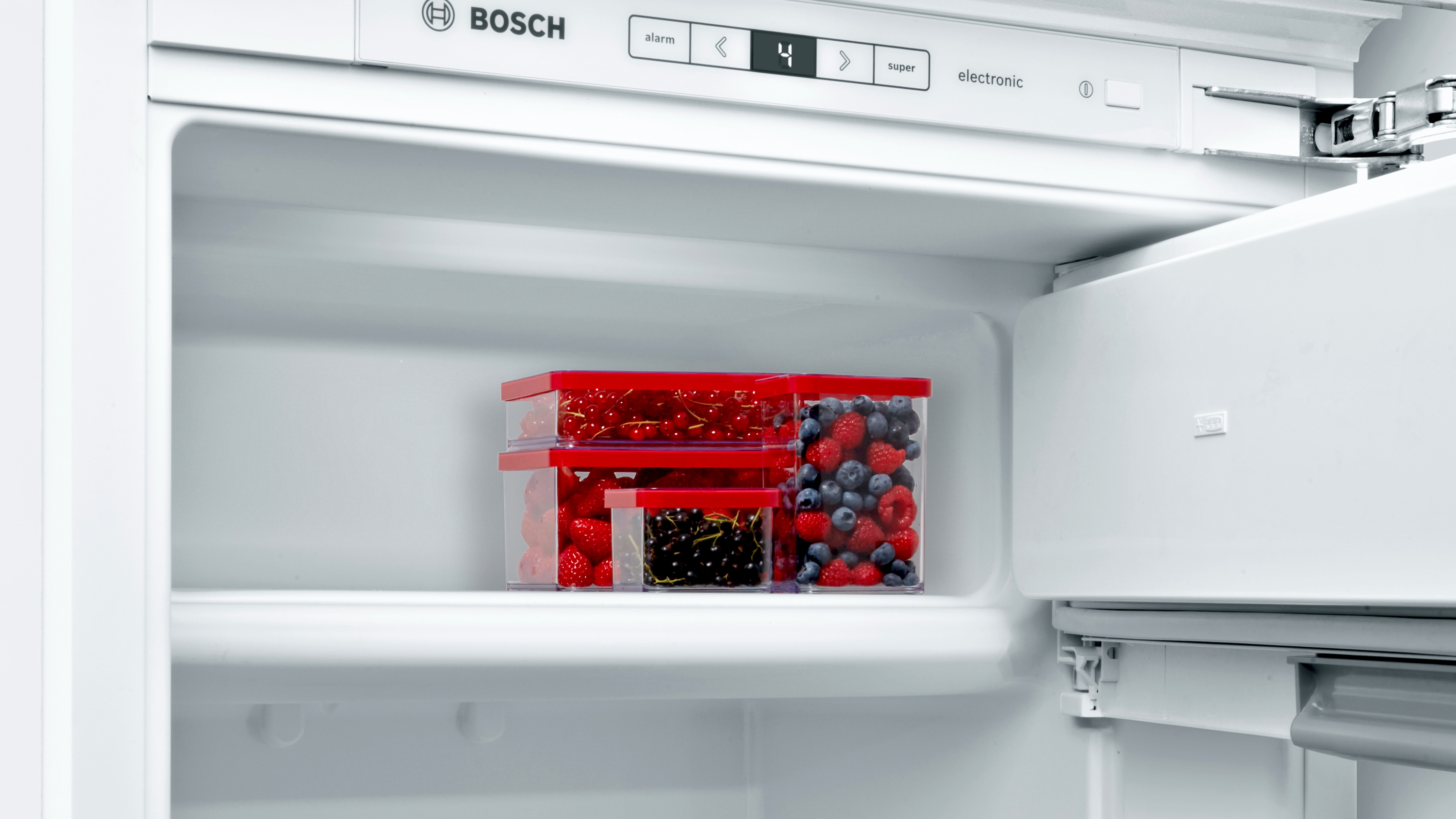 Kühlschrank mit drei Behältern mit Beeren im Inneren. Weiße Innenausstattung, rote und transparente Behälter.