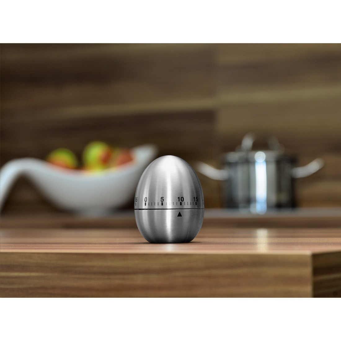 Stainless steel egg timer with dial on a wooden surface near a bowl and pot.