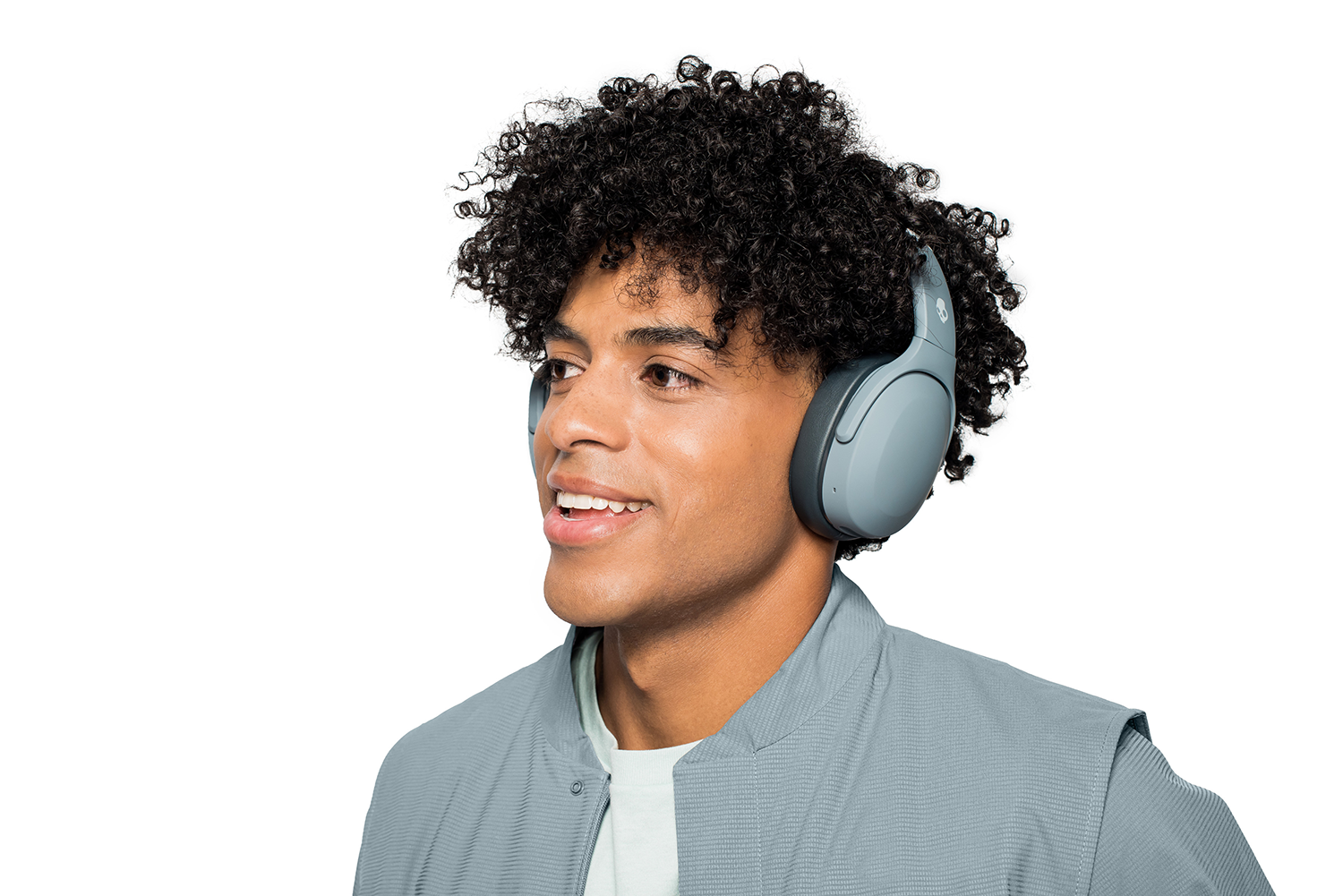 A young man wearing gray headphones, smiling on a white background.