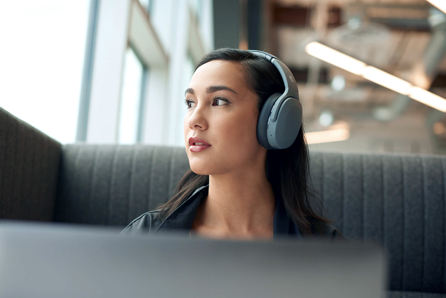 Woman wearing grey headphones looking out a window, blurred background.