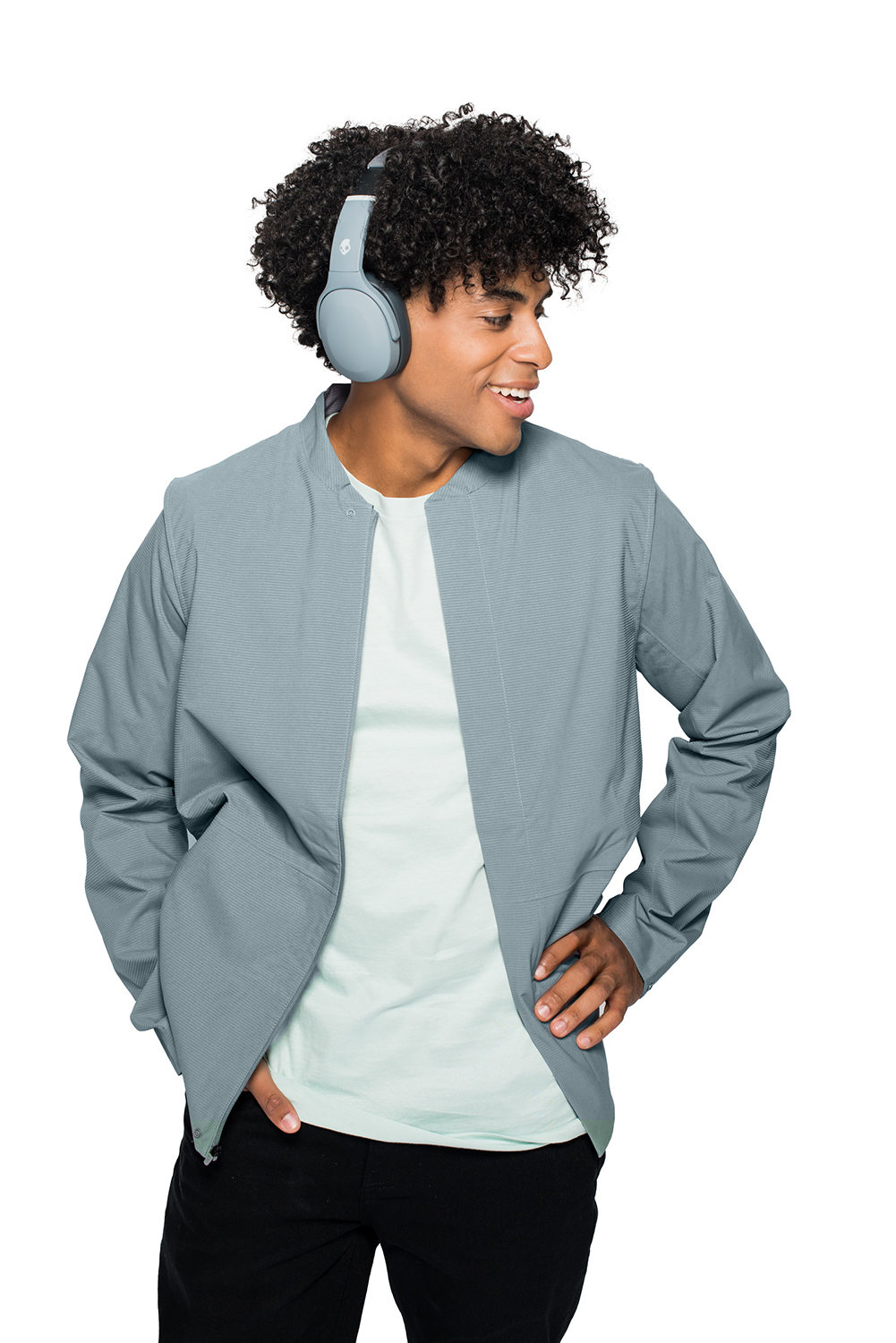 A young man wearing gray headphones and a light blue jacket, smiles, looking to the side.