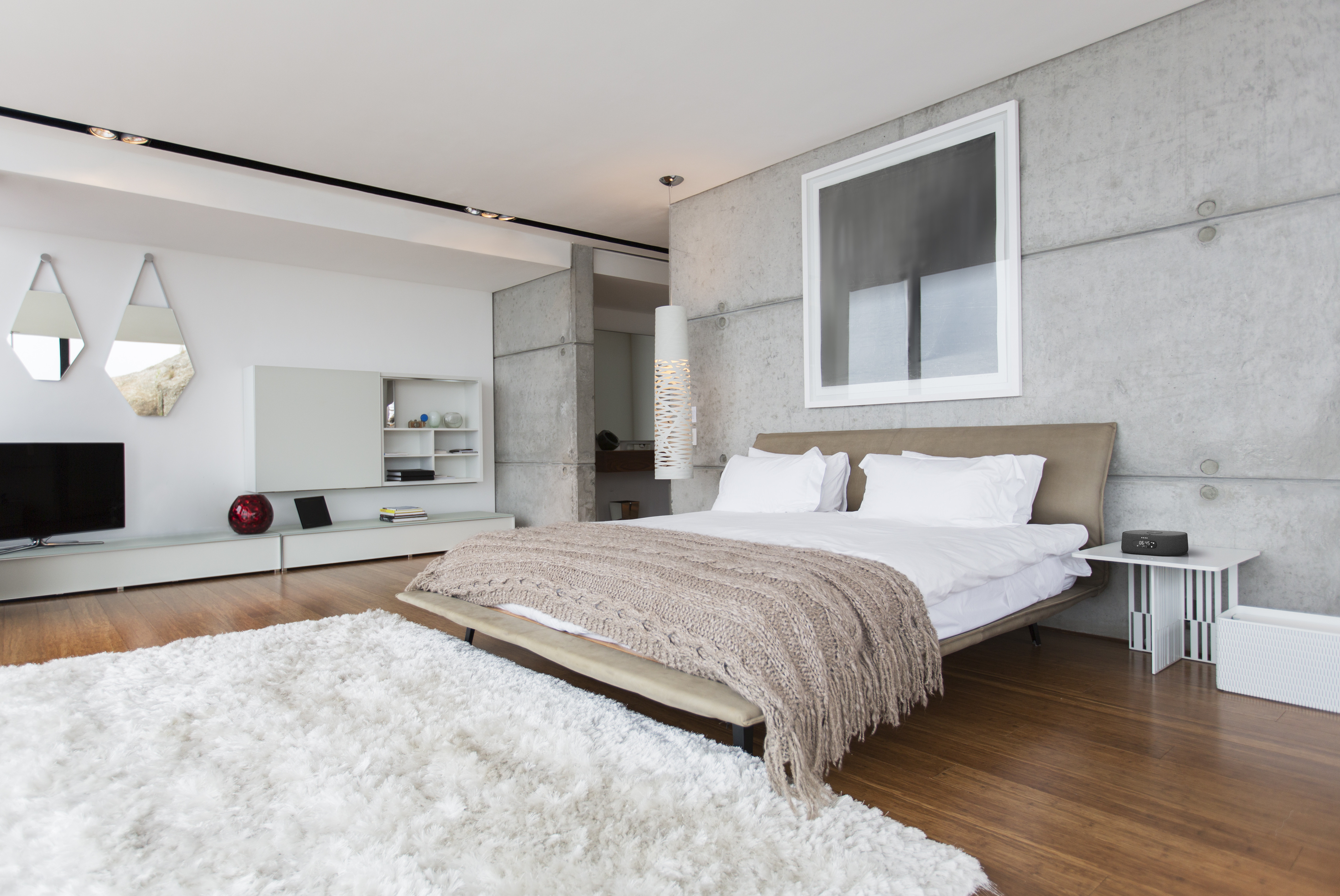 Moderne slaapkamer met een bed, vloerkleed en groot kunstwerk. Grijze betonnen muur en een wit plafond.