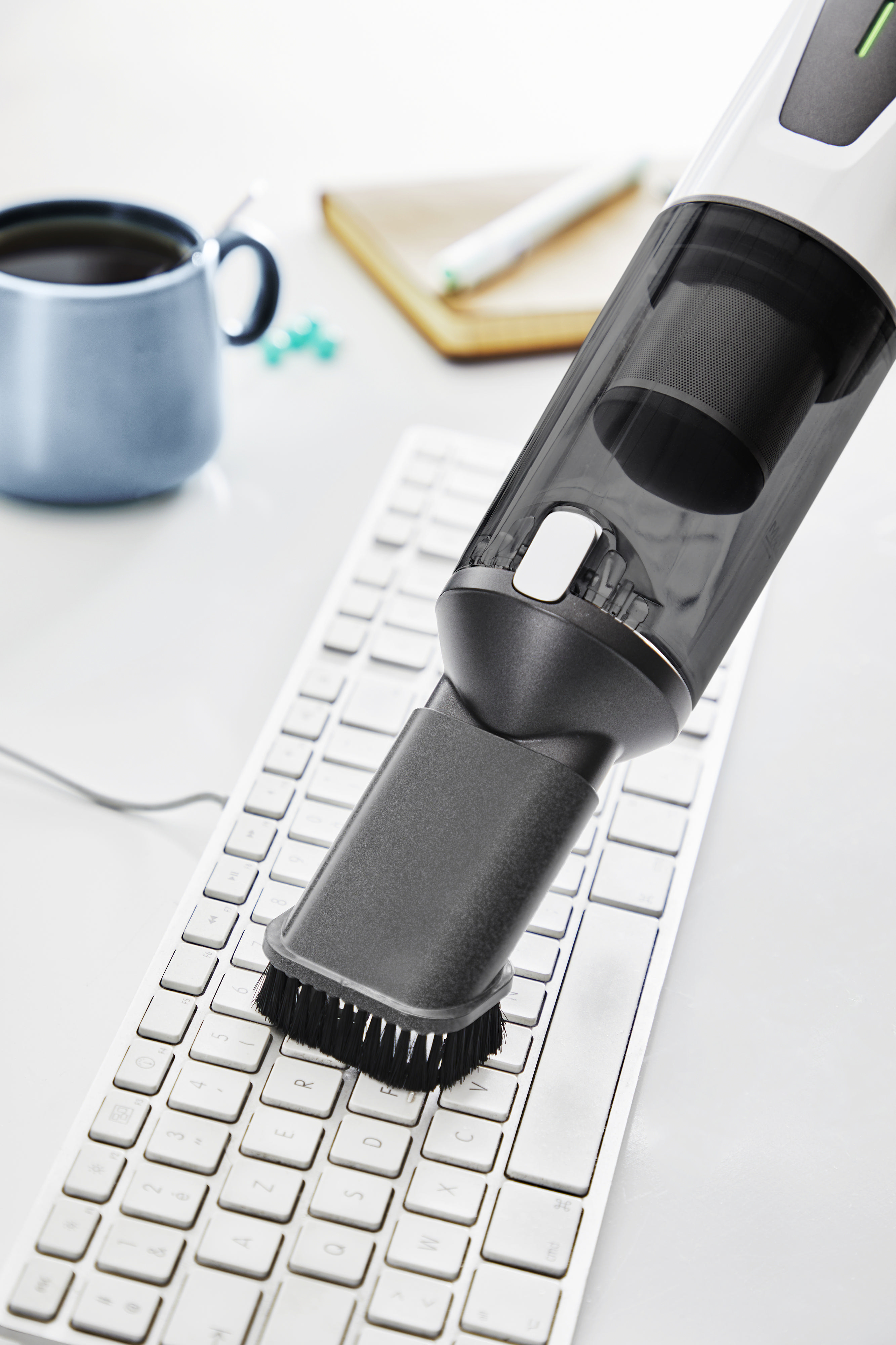 Ein Handstaubsauger reinigt eine Tastatur, daneben eine Kaffeetasse.