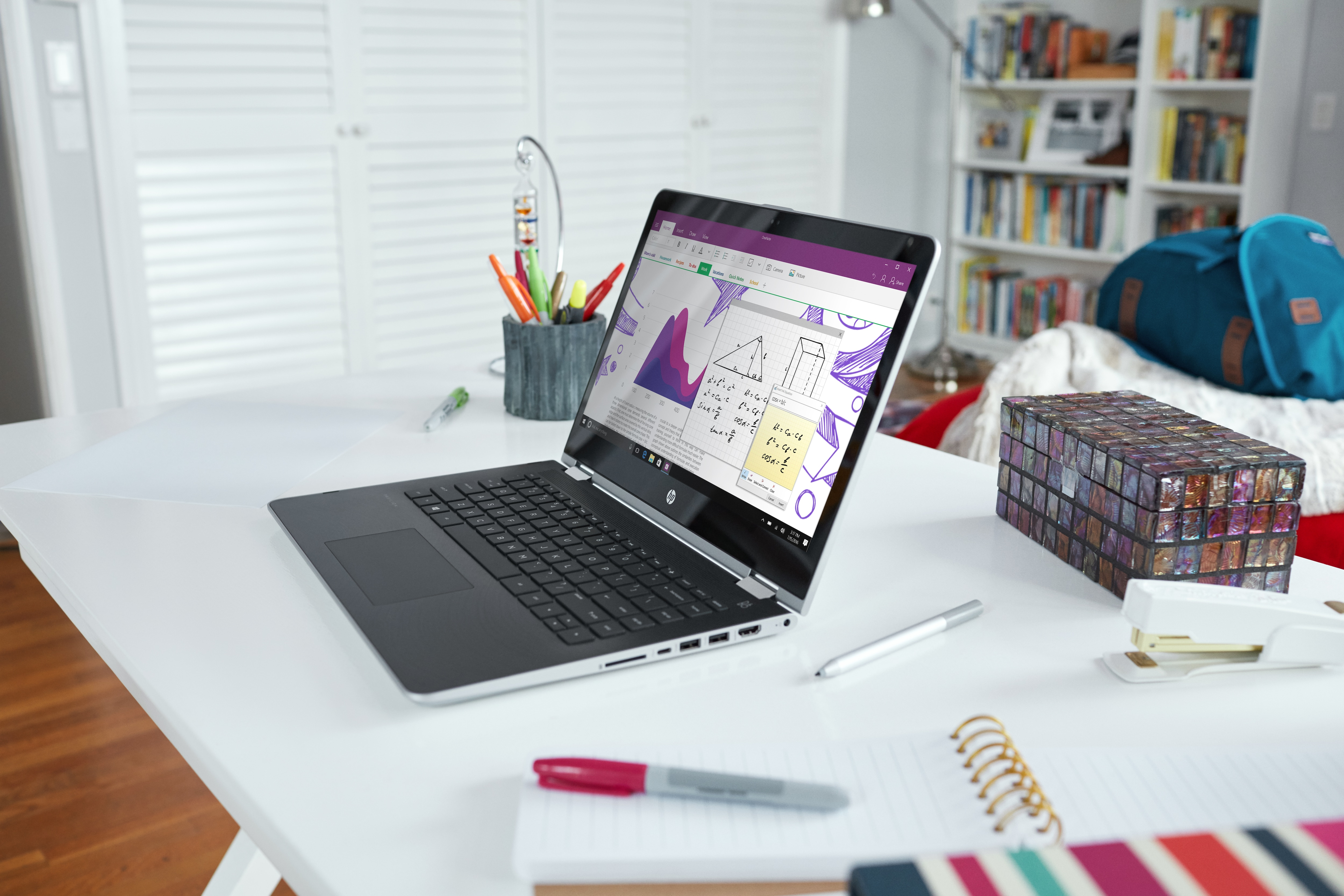 Ein offener Laptop auf einem weißen Schreibtisch zeigt Matheformeln und Diagramme auf dem Bildschirm.