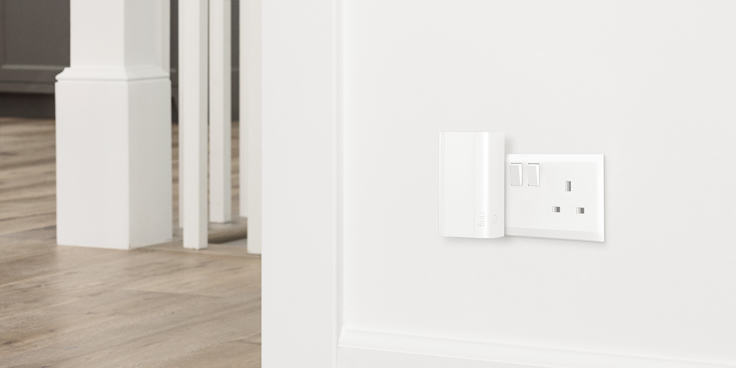 A white smart home device plugged into a white wall outlet.