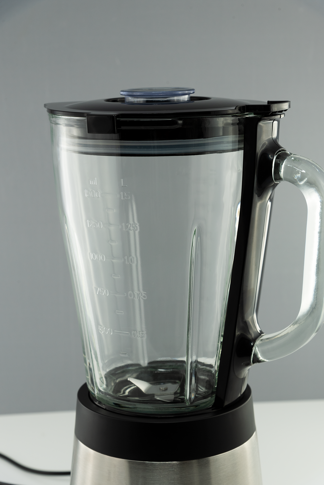 Ein durchsichtiger Glas-Mixbehälter mit Messmarkierungen, der auf einem schwarzen Sockel steht.