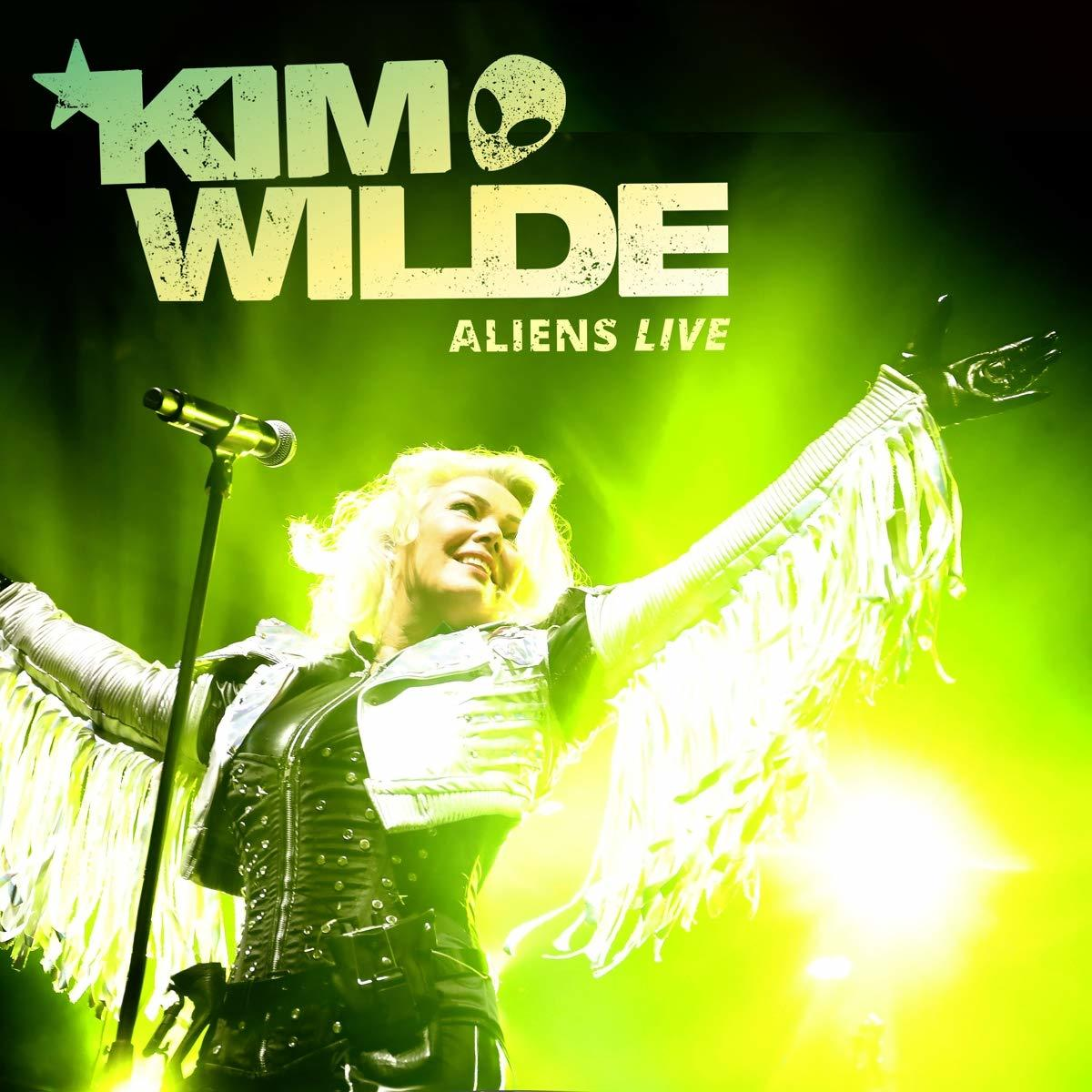 Kim Wilde auf der Bühne mit ausgestreckten Armen. Grüner Hintergrund mit weißem Text 'Aliens Live'.
