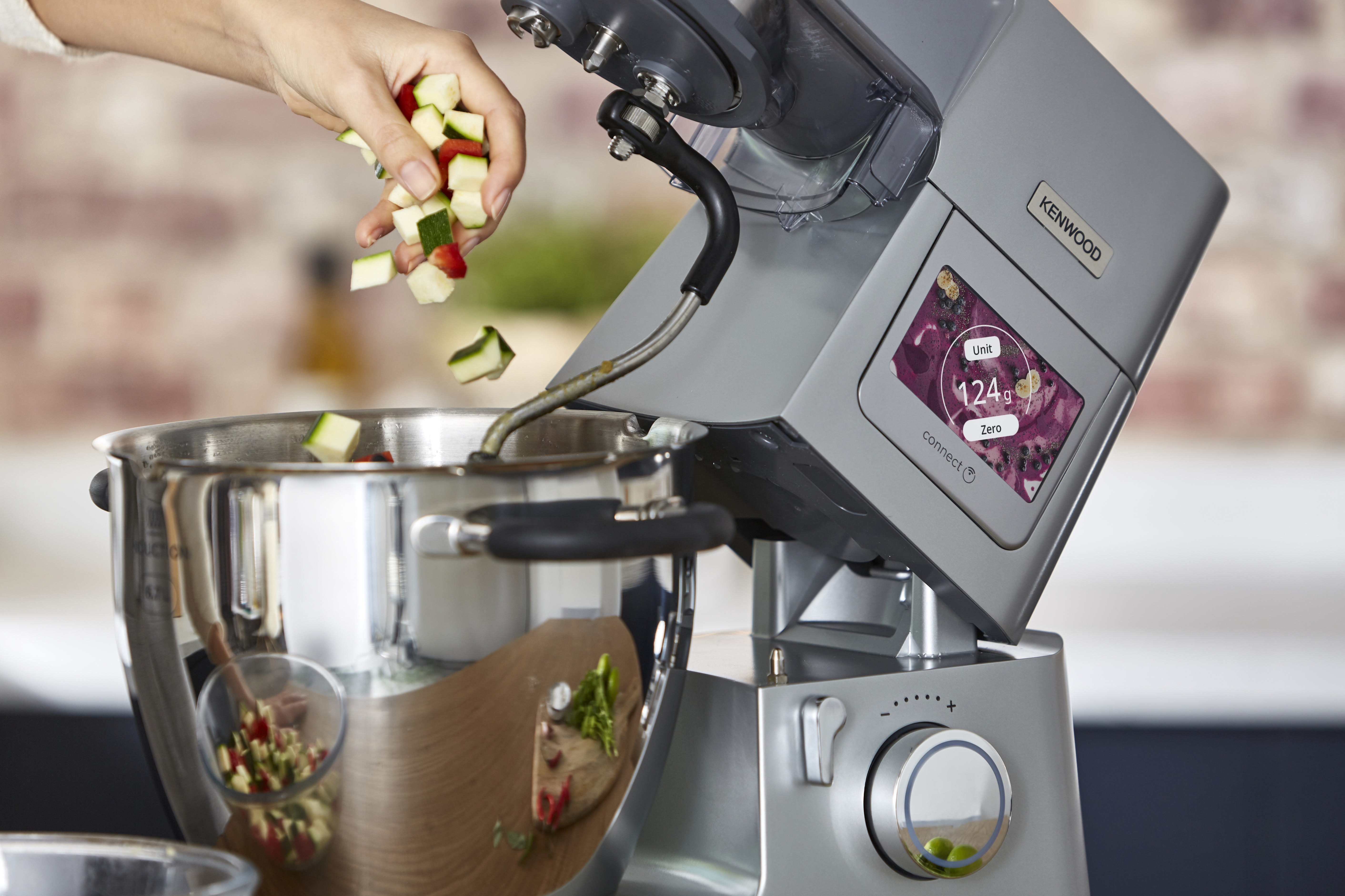 Frau gießt gehacktes Gemüse in eine Rührschüssel, die an einem Küchenmixer befestigt ist.