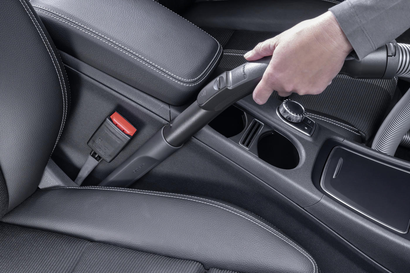 Hand, die einen Staubsauger im Auto verwendet, konzentriert sich auf die Konsole und den Gurt.