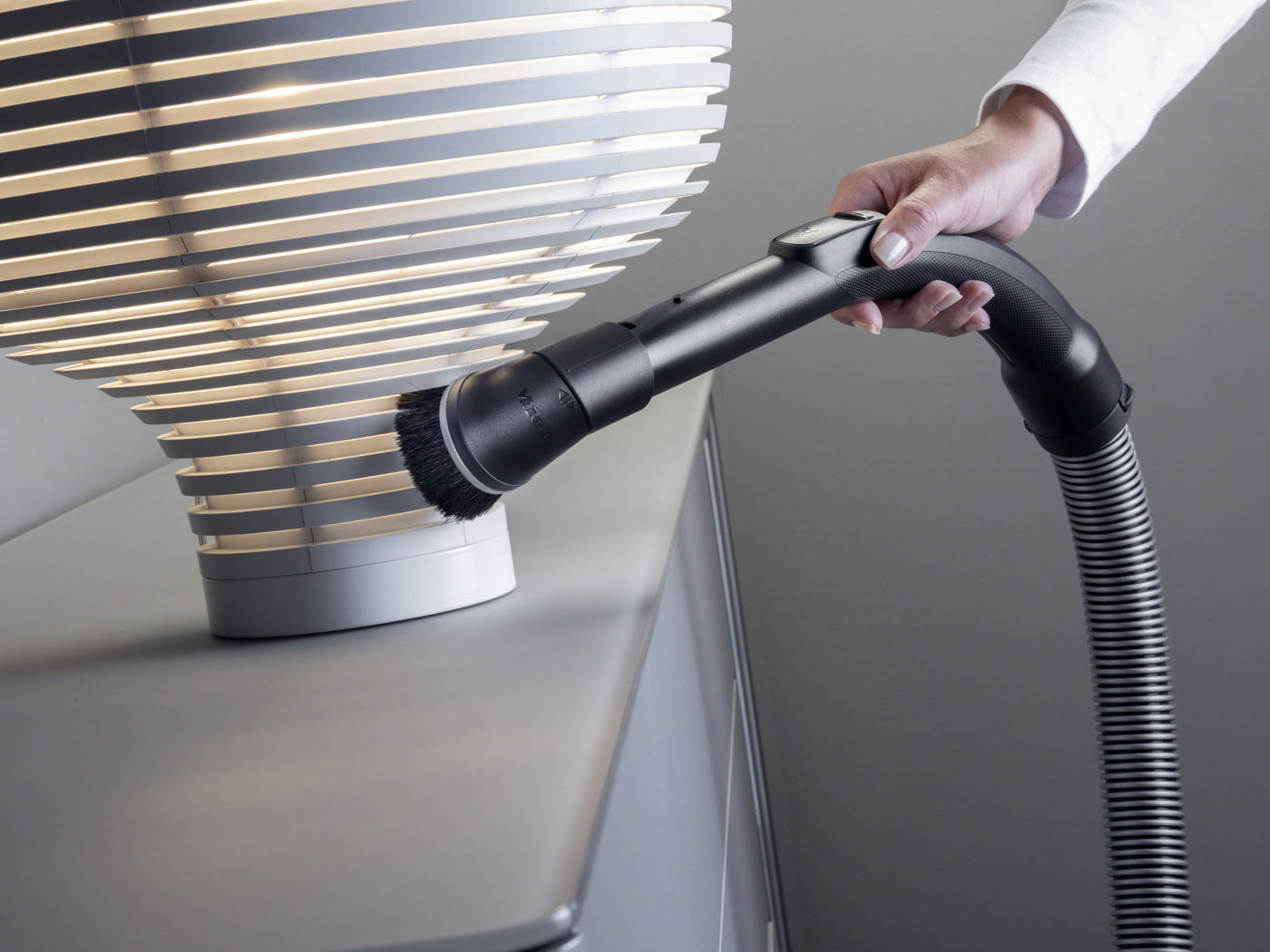 Die Hand einer Person, die einen Staubsaugeraufsatz zum Reinigen einer Lampe verwendet.