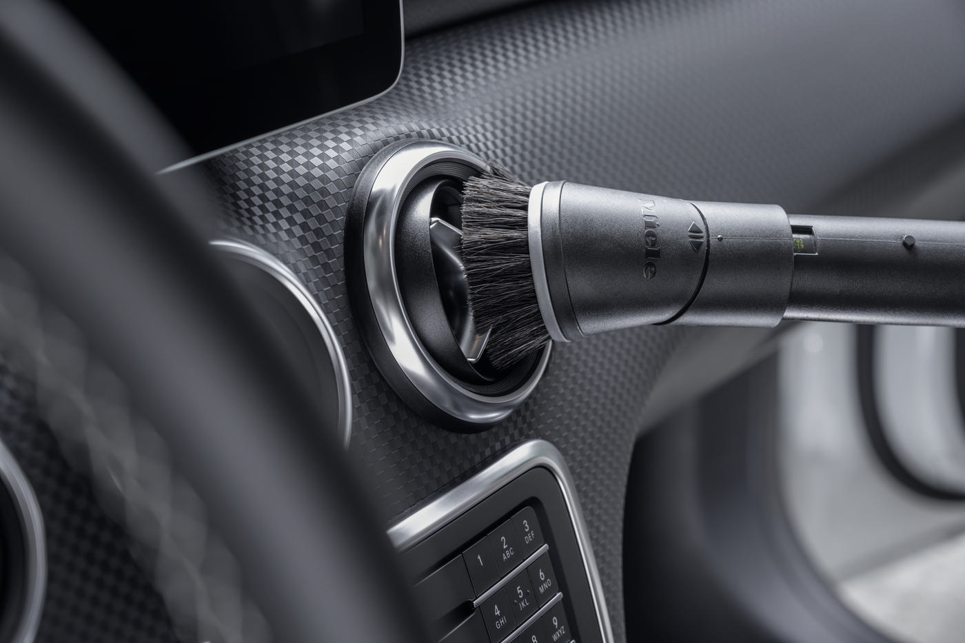 Detail eines Auto-Luftauslasses, der mit einem Bürstenaufsatz gereinigt wird.