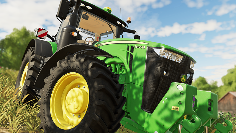 Een groene en gele John Deere tractor. De achtergrond is gras en bomen.