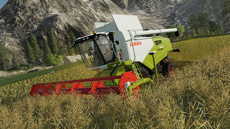 Een CLAAS combine harvester in een graanveld, met bergen op de achtergrond. De lucht is blauw.
