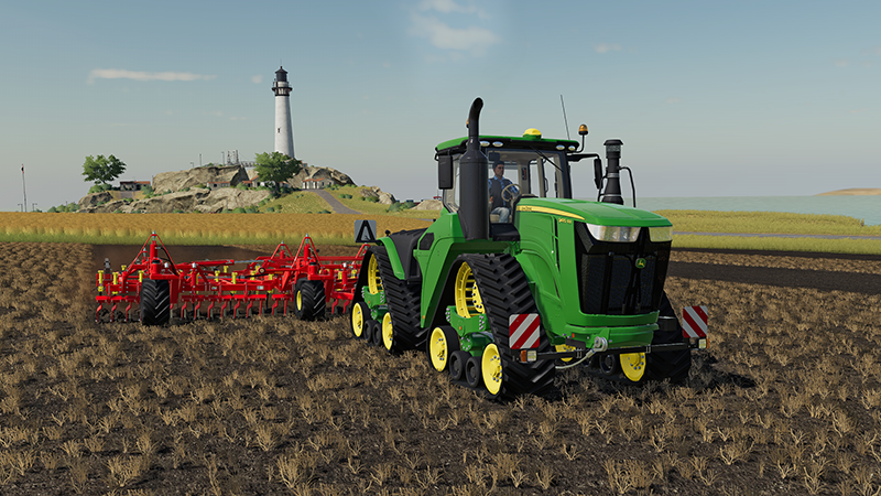 Een groene tractor met een rode ploeg in een veld, met een vuurtoren op de achtergrond.