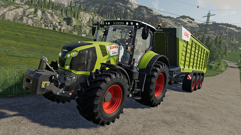 Groene Claas Axion-trekker trekt een aanhanger op een weg in een landelijk landschap.