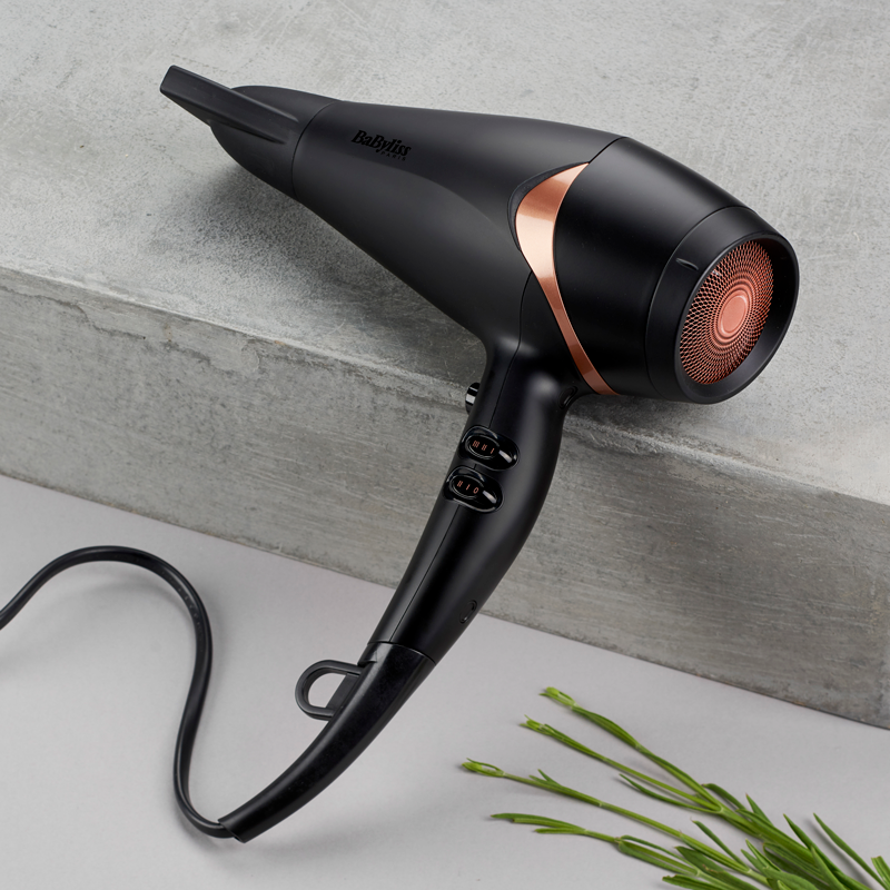 Un sèche-cheveux noir et or rose sur une surface grise.