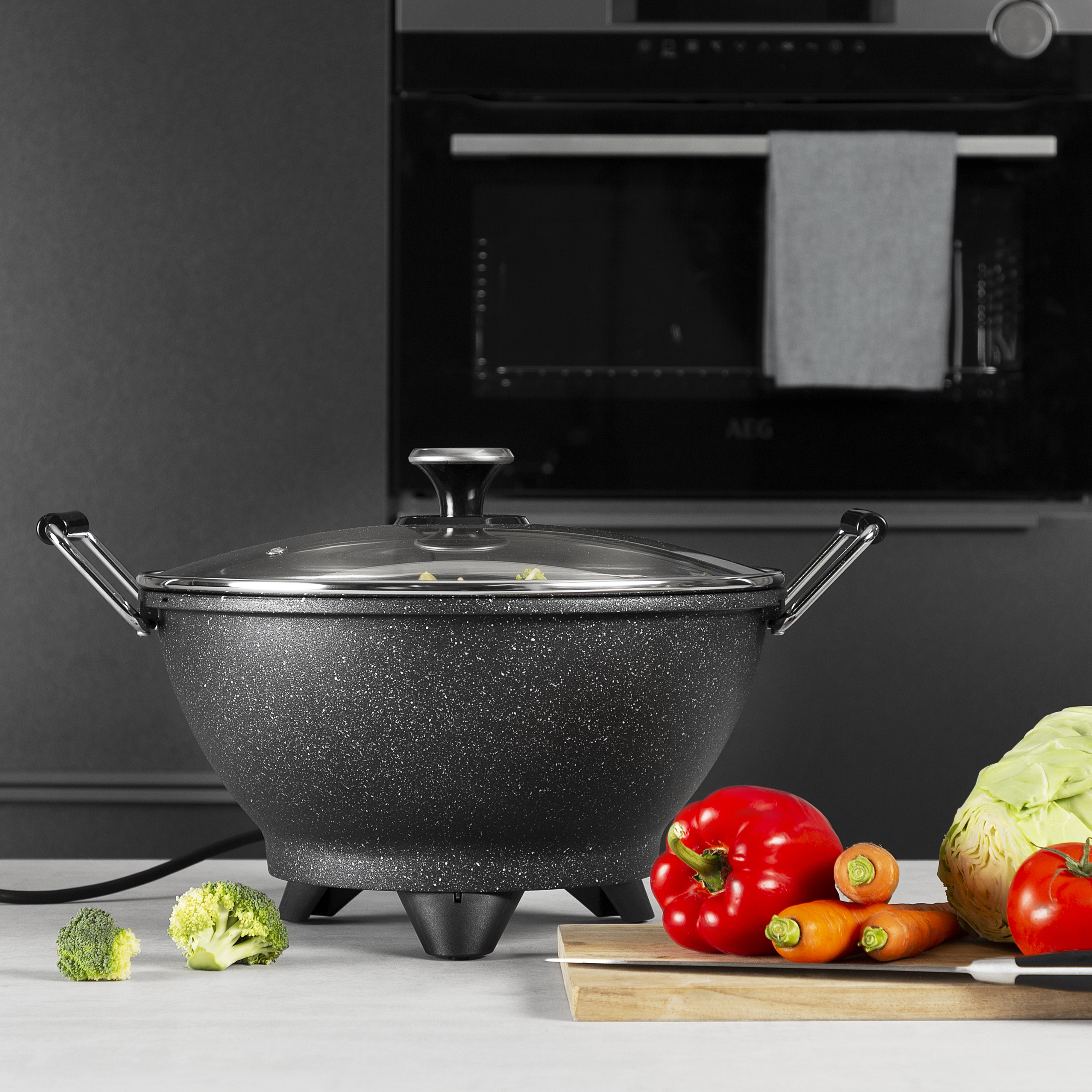 Wok with vegetables and a cutting board on a kitchen counter. Dark background.