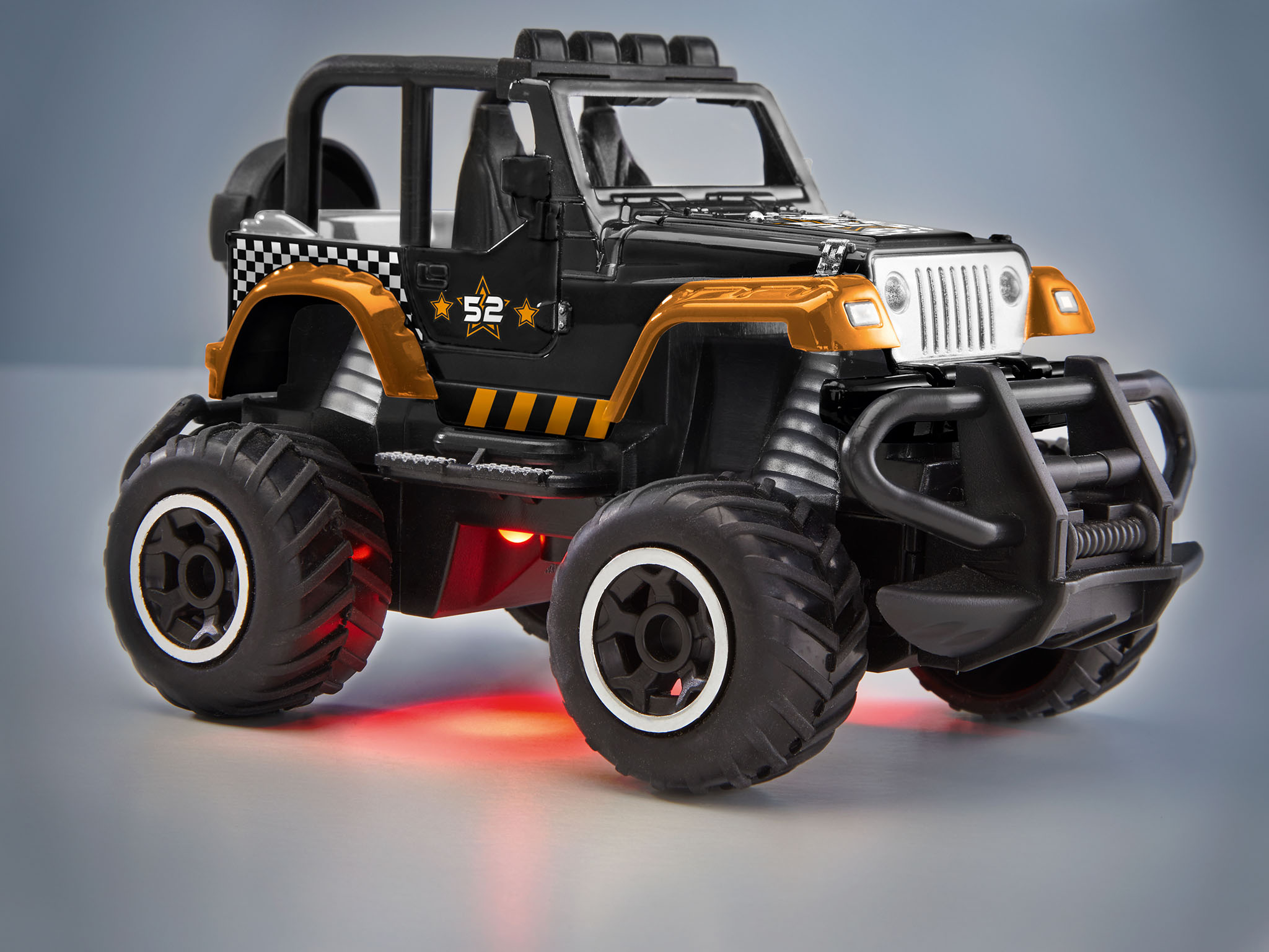 Ein schwarz-oranger Spielzeug-Jeep mit großen Reifen und roten Lichtern auf grauer Oberfläche.