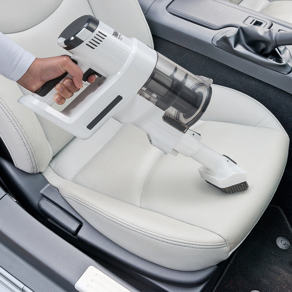 Hand hält einen weißen, kabellosen Staubsauger und reinigt einen weißen Autositz.