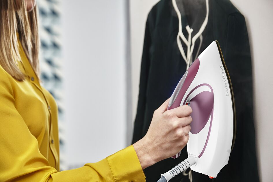 A woman ironing a dark green garment with a white and maroon iron, yellow shirt.