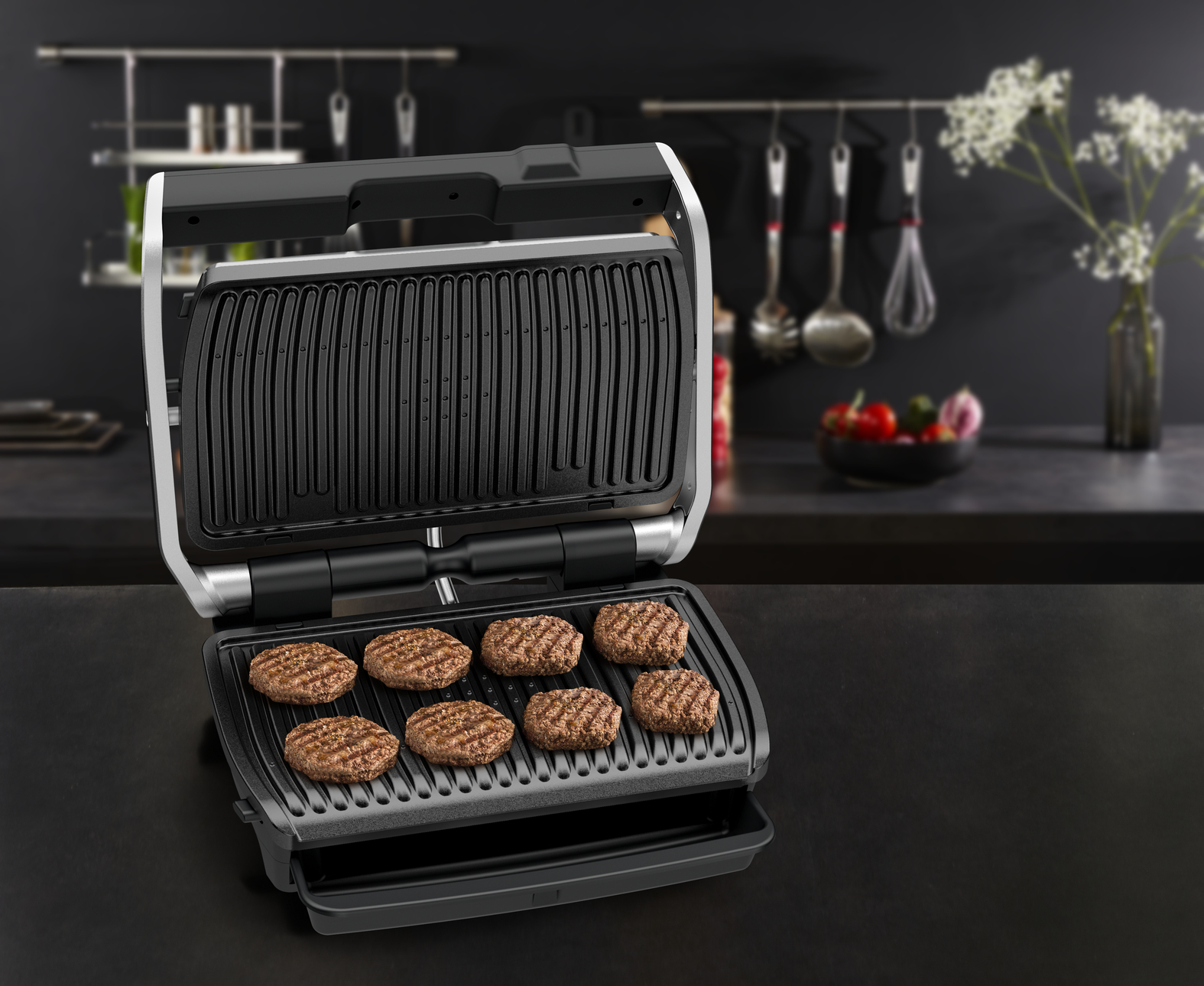 A grill with burgers cooking inside, on a black surface. Kitchen background is blurred.
